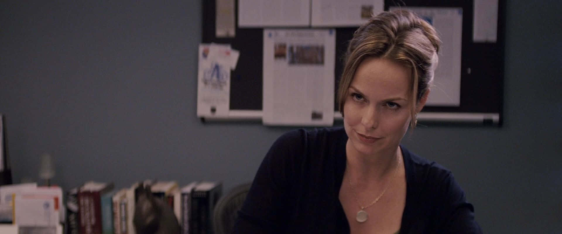 Melora Hardin 桌布 壁紙 — 一位頭髮造型時尚的女性坐在辦公椅上，直視鏡頭，表情嚴肅。