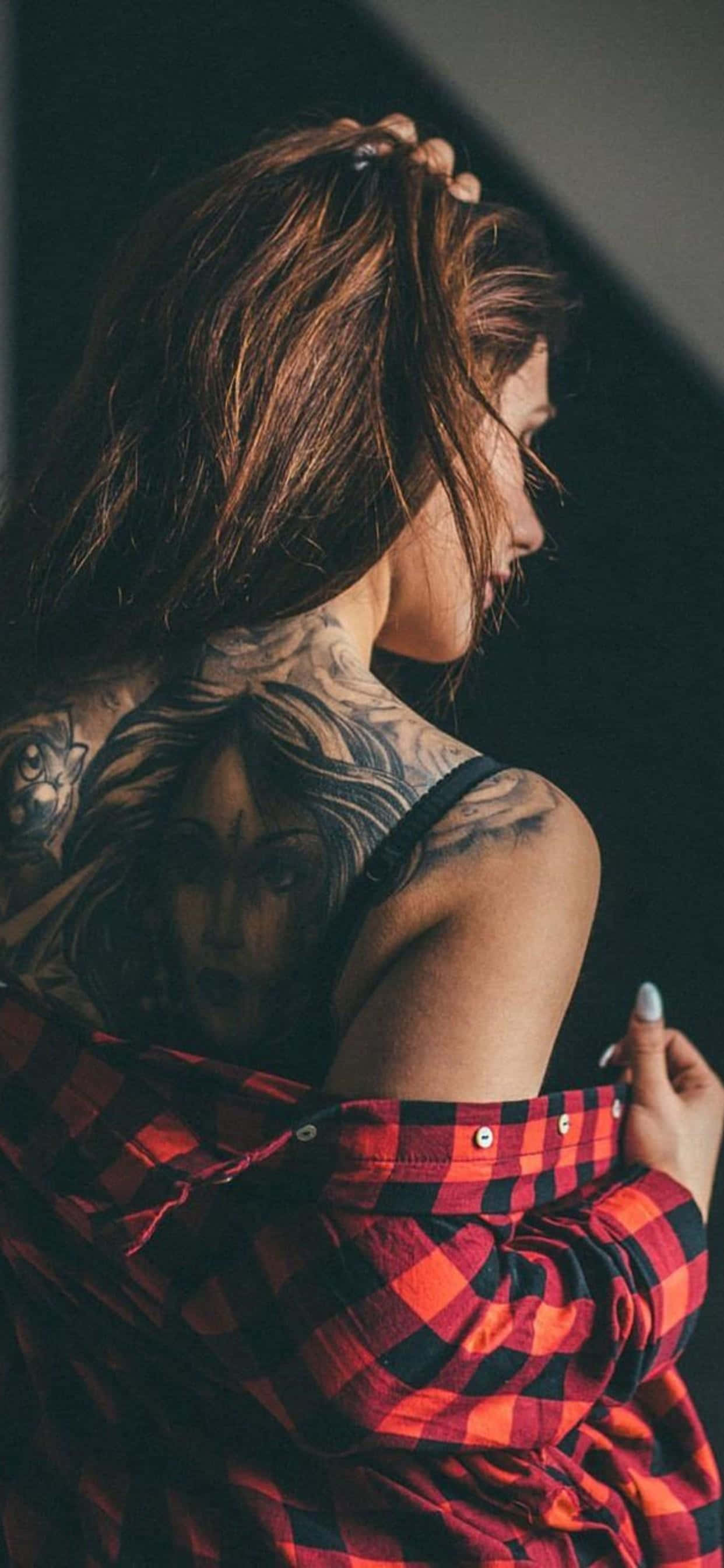 Tattoo Girl 桌布 壁紙 — 一位頸部和肩部有複雜刺青的女性，穿著紅色格子襯衫，目光望向遠方。