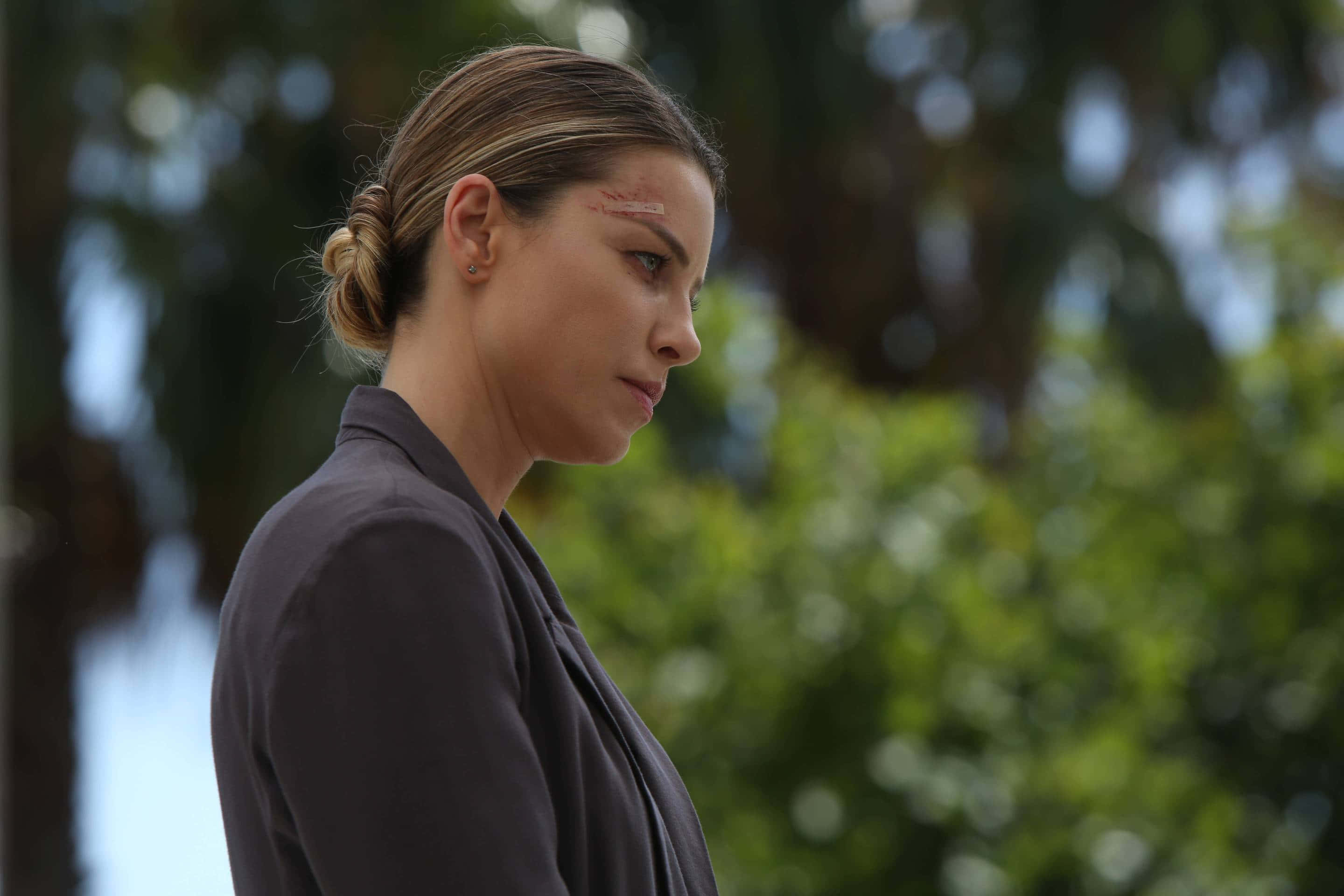 Lauren German 桌布 壁紙 — 一位額頭有割傷的女性側面站立，背景是模糊的綠色戶外環境。