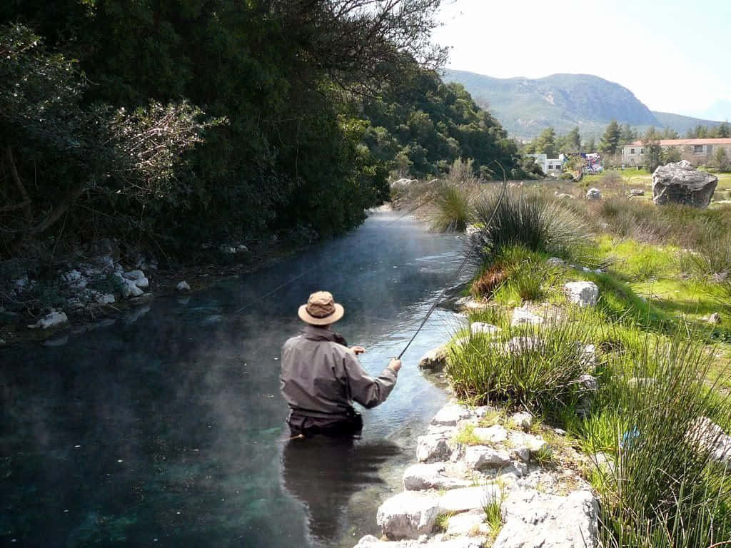 一名男子在山間溪流釣魚，戴著帽子，在清澈的水中涉水。 — 釣魚 GIF 壁紙
