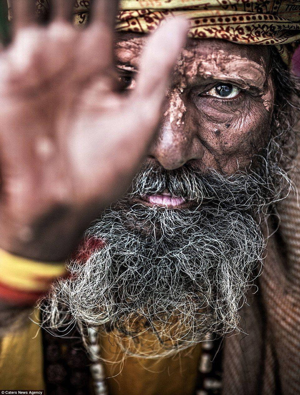 Aghori 桌布 壁紙 — 一位飽經風霜的男士的頭像特寫，留著長長的灰色鬍鬚，戴著圖案頭巾，他的手舉在臉前。
