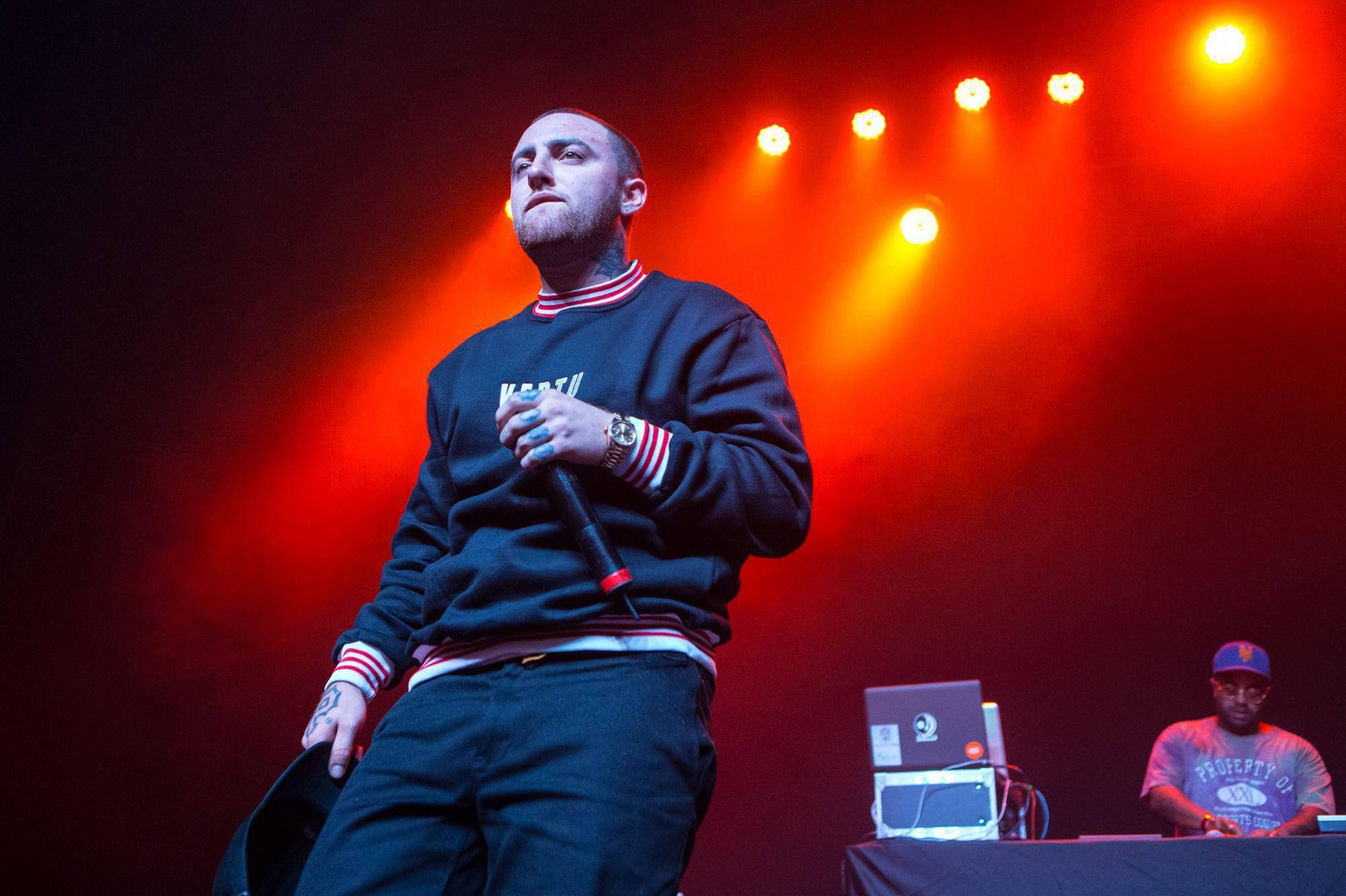 Mac Miller 桌布 壁紙 — 一位饒舌歌手在強烈的紅色聚光燈下於舞台上表演，背景中可見一名DJ。