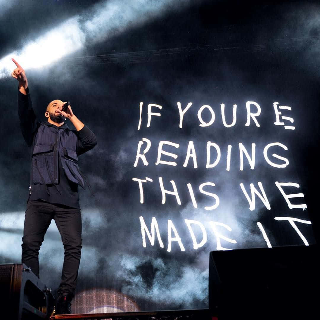 Drake 桌布 壁紙 — 一位饒舌歌手在明亮的燈光、煙霧和一個顯示「if youre reading this we made it」的大螢幕下於舞台上表演。