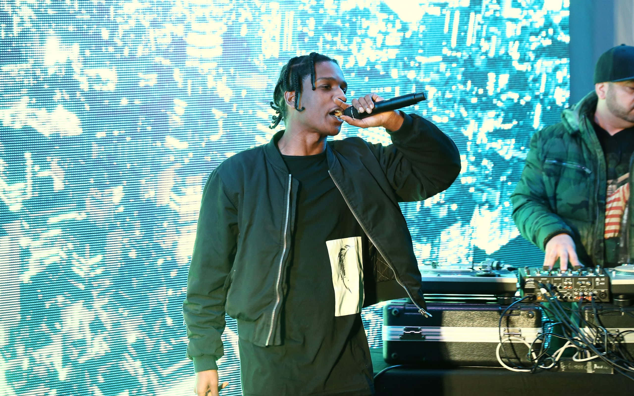 ASAP Rocky 桌布 壁紙 — 一位饒舌歌手在舞台上熱情表演，背後有發光的藍色數位背景，旁邊有一位DJ。