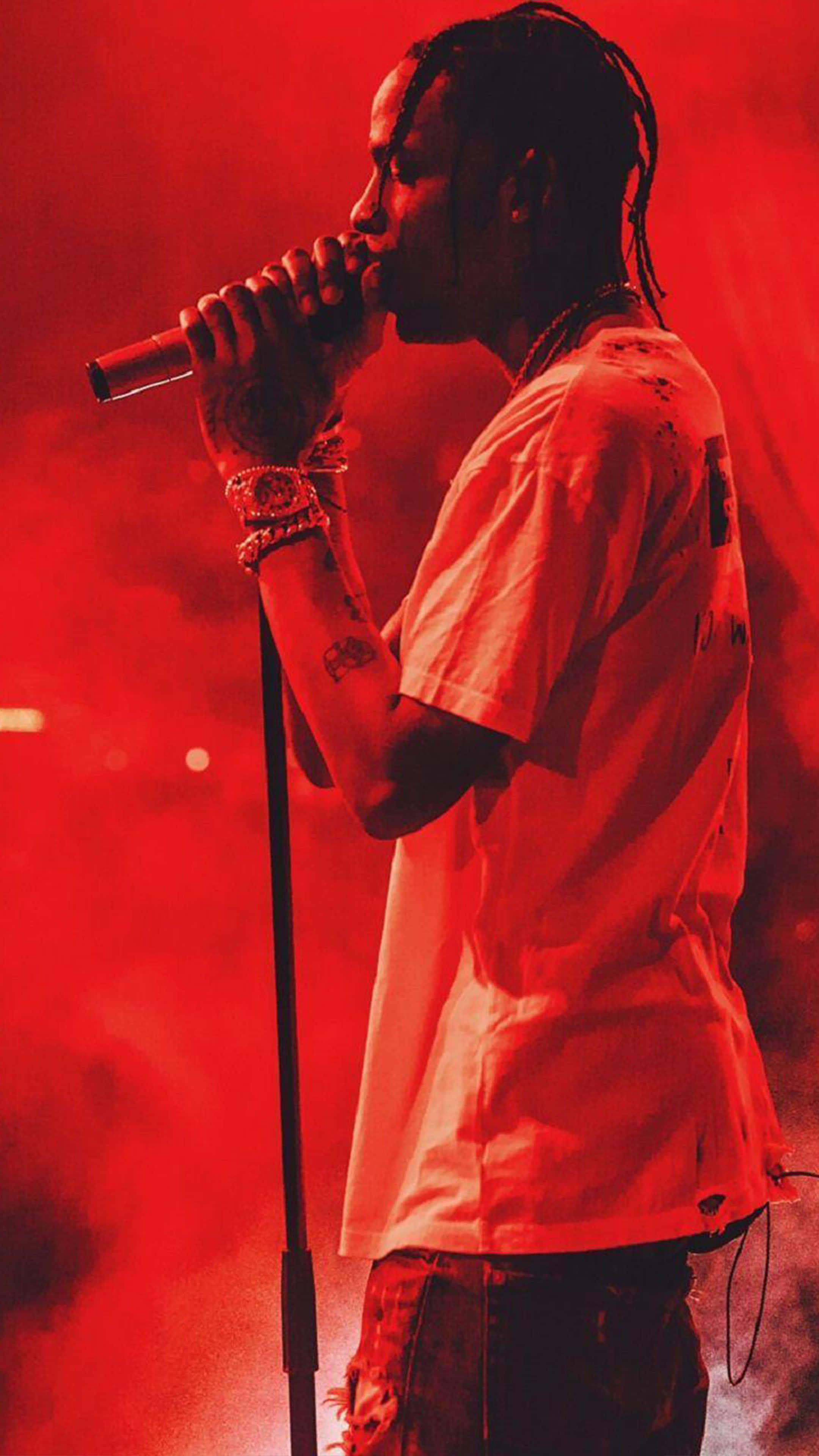 Travis Scott Concert 桌布 壁紙 — 一位饒舌歌手在舞台上表演，被強烈的紅光照耀，煙霧在他周圍旋轉。