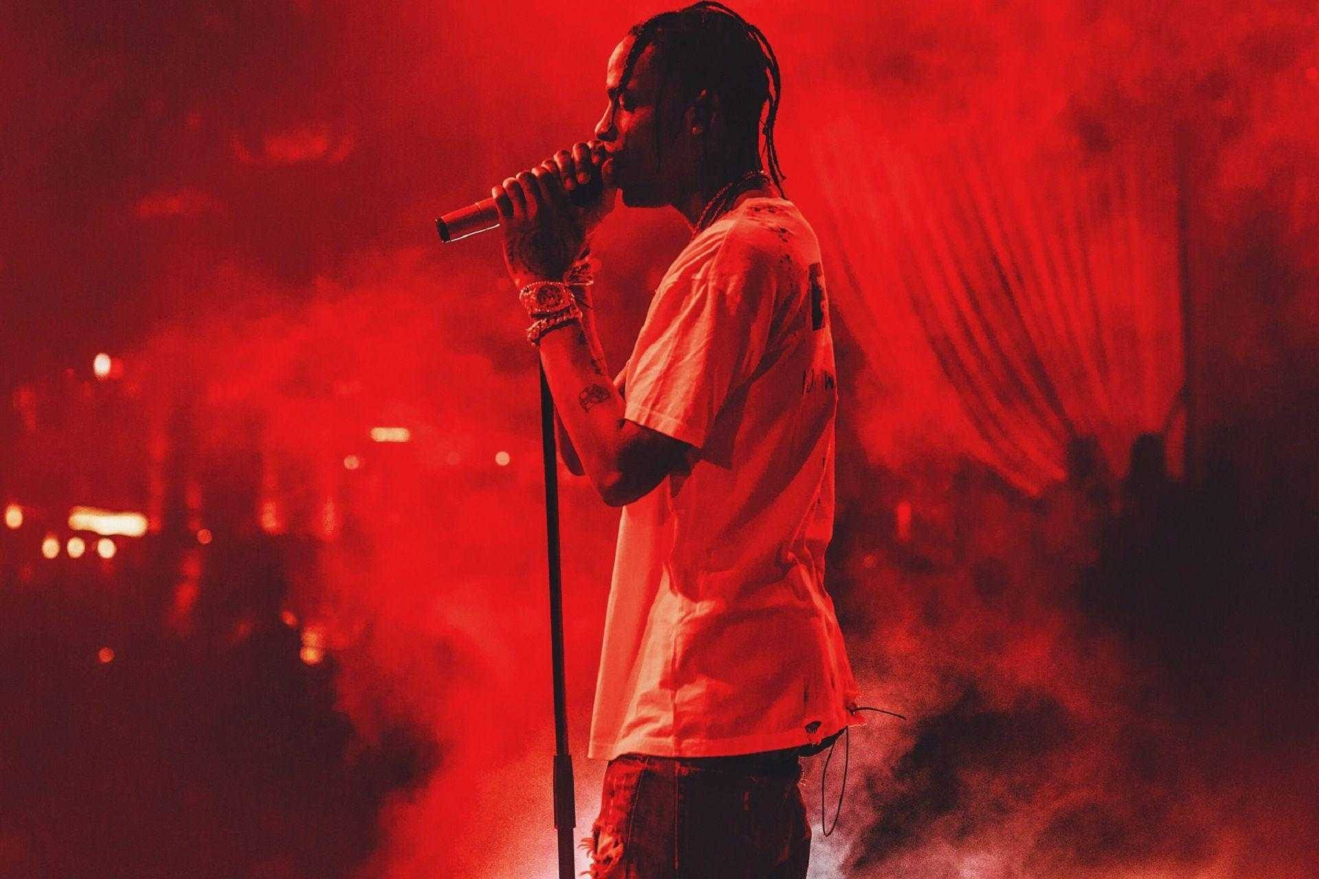 Travis Scott Aesthetic 桌布 壁紙 — 一位饒舌歌手在舞台上表演，被強烈的紅光和煙霧籠罩，手中拿著麥克風。
