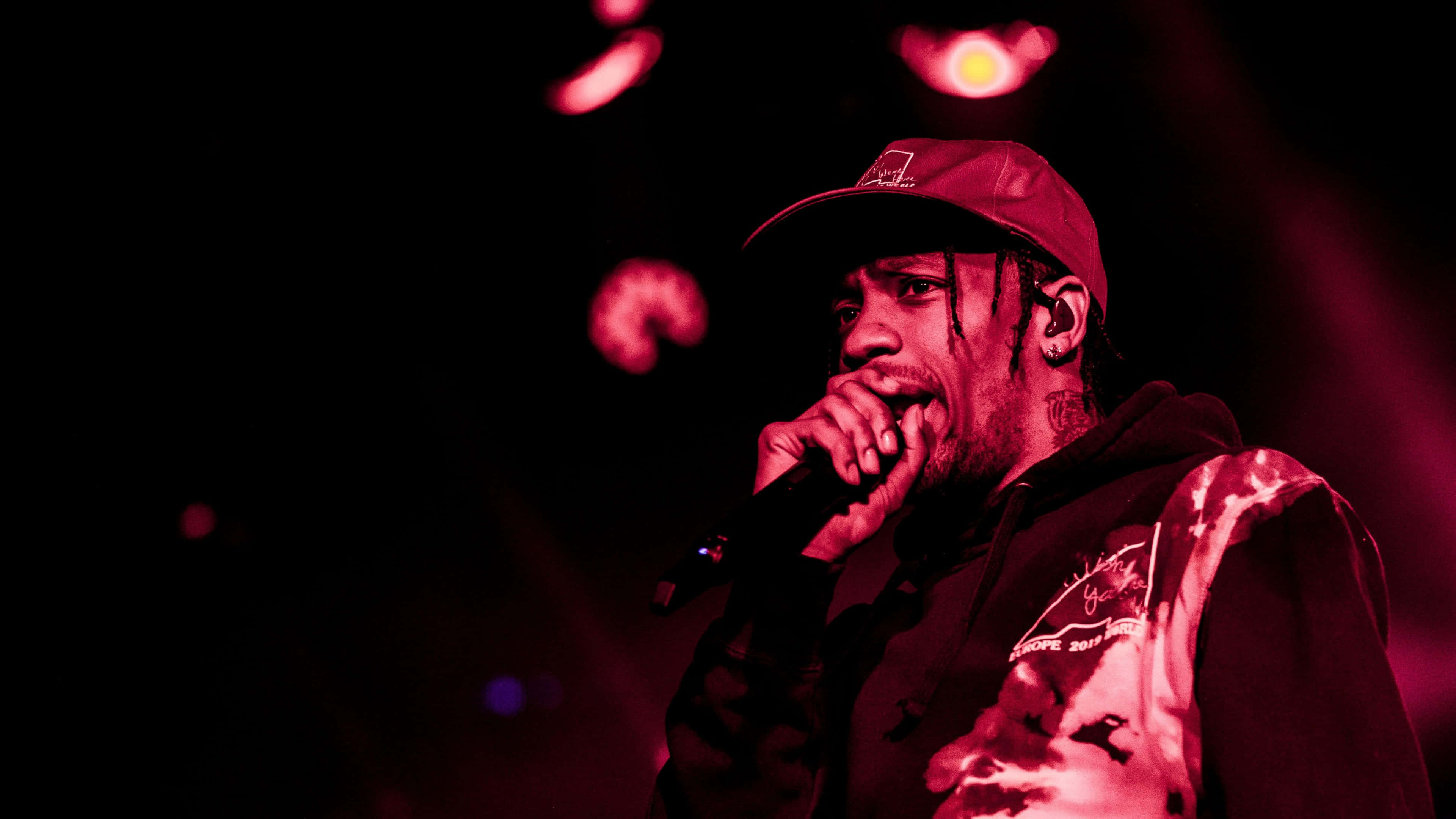 Travis Scott Concert 桌布 壁紙 — 一位饒舌歌手在舞台上表演，身後沐浴在強烈的紅光中，帶有發光的散景效果。