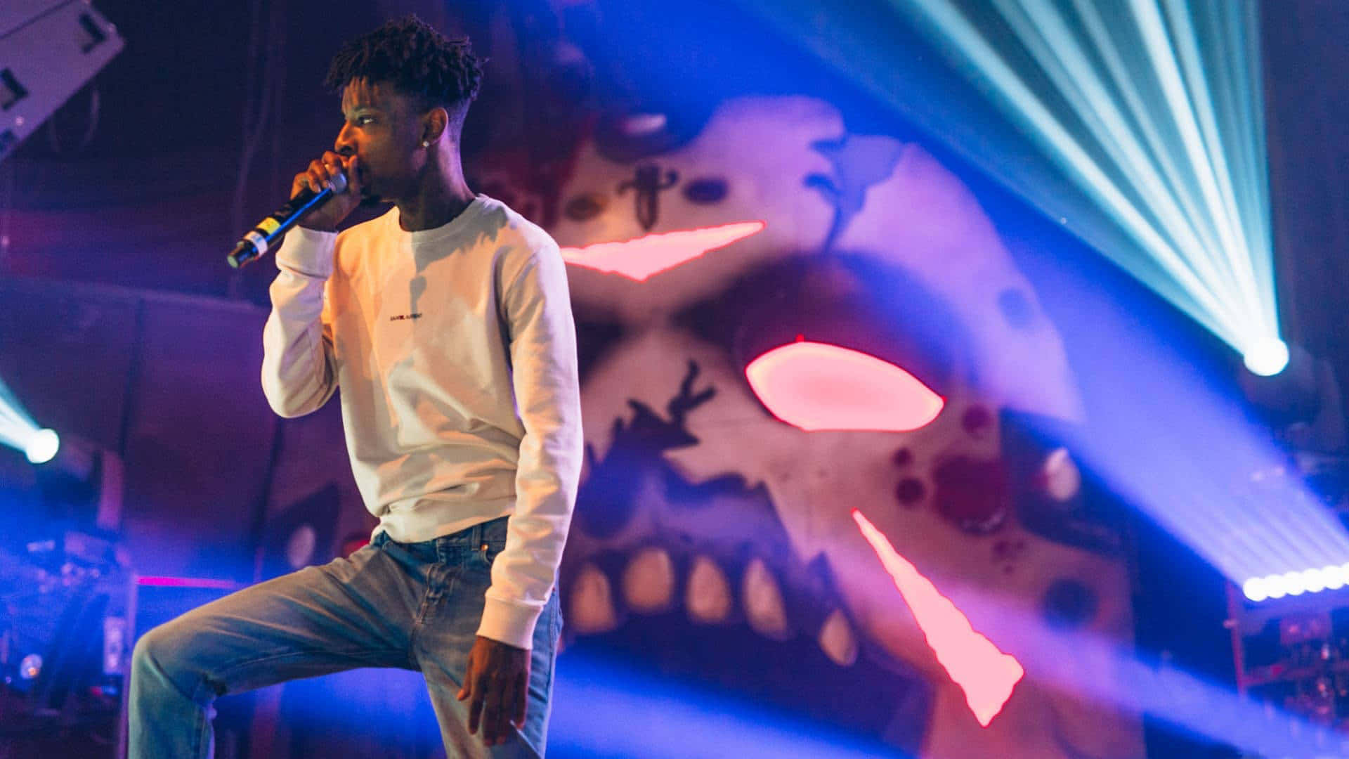 21 Savage 桌布 壁紙 — 一位饒舌歌手在藍色燈光下，以發光骷髏背景在舞台上表演。