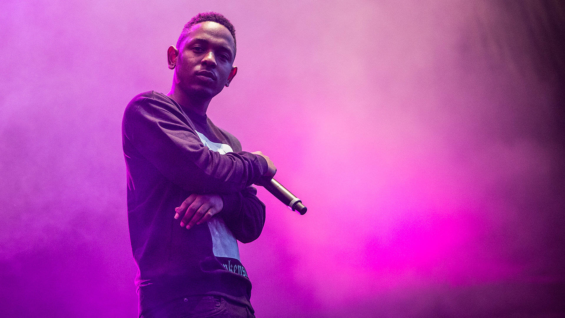 Kendrick 桌布 壁紙 — 一位饒舌歌手自信地站在舞台上，在充滿活力的紫色舞台燈光和煙霧中手持麥克風。