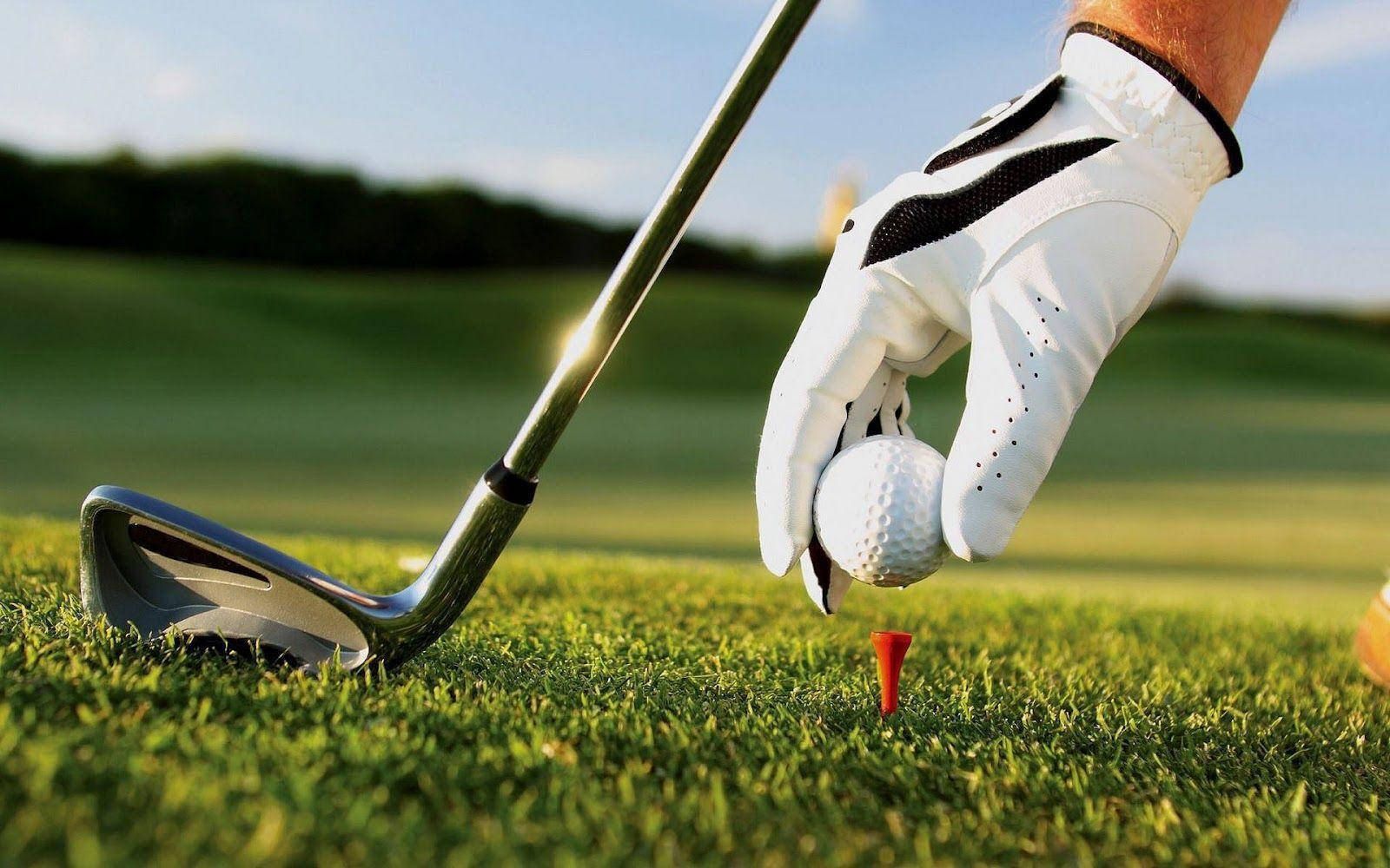 Golfing 桌布 壁紙 — 一位高爾夫球手戴著手套的手將一個白色高爾夫球放在紅色球座上，球座位於陽光普照的綠色球道上，附近放著一支球桿。