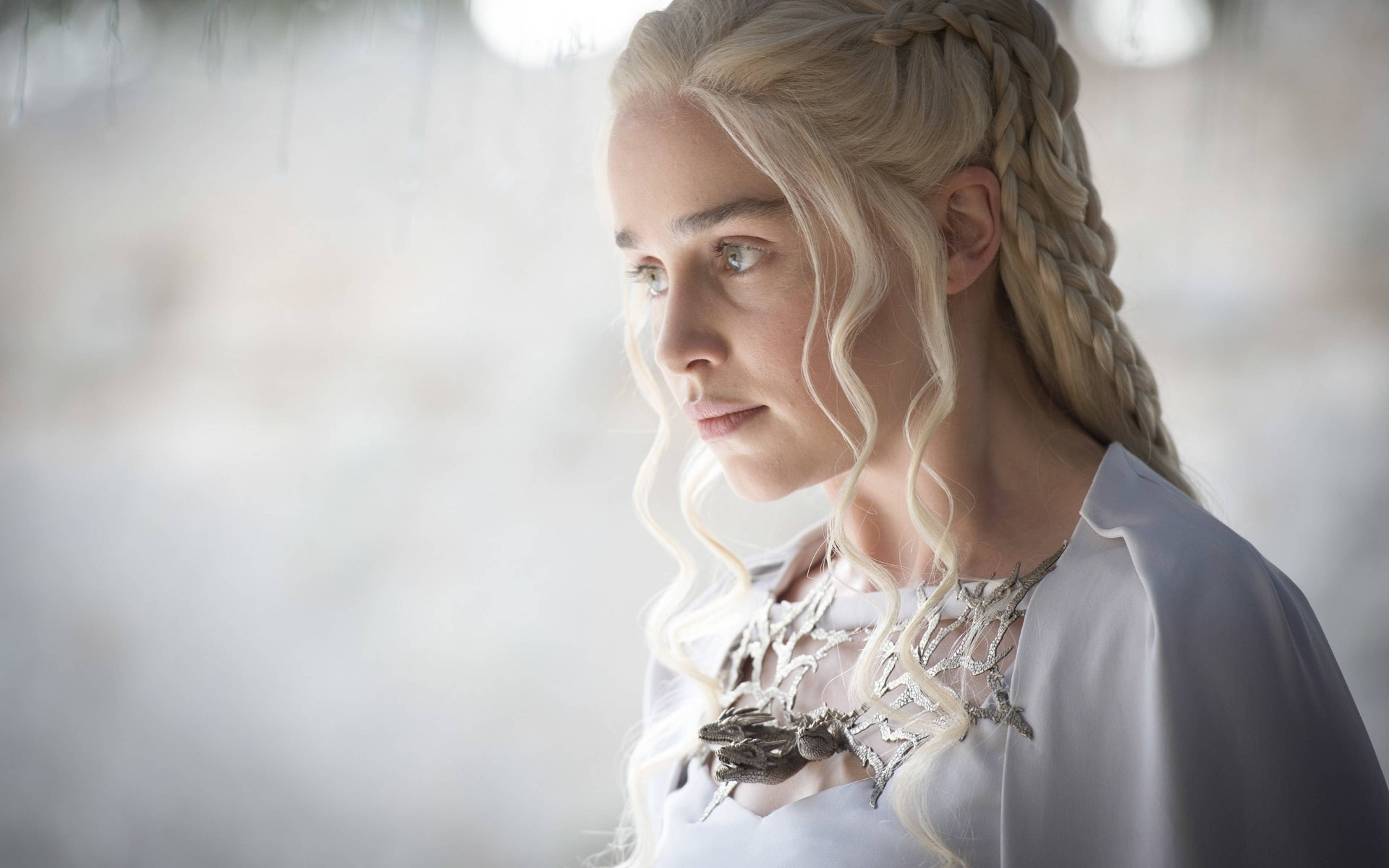 daenerys 桌布 壁紙 — 一位高貴的金髮女子，編著辮子，在柔和日光下若有所思地凝視，戴著華麗的銀飾和白色長袍。