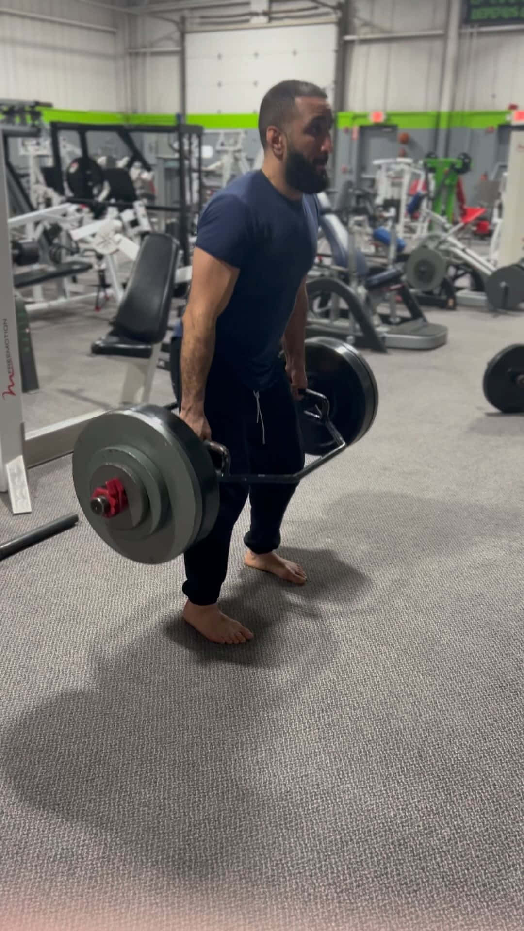 Fitness 桌布 壁紙 — 一位鬍鬚男在健身房赤腳於灰色地毯上進行硬舉訓練，用力舉起沉重的槓鈴。