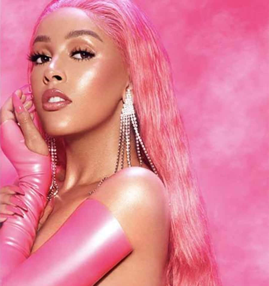 Doja Cat 桌布 壁紙 — 一位魅力四射的女士，留著長長的粉紅色頭髮，戴著相配的粉紅色手套，在充滿活力的粉紅色背景前擺姿勢。