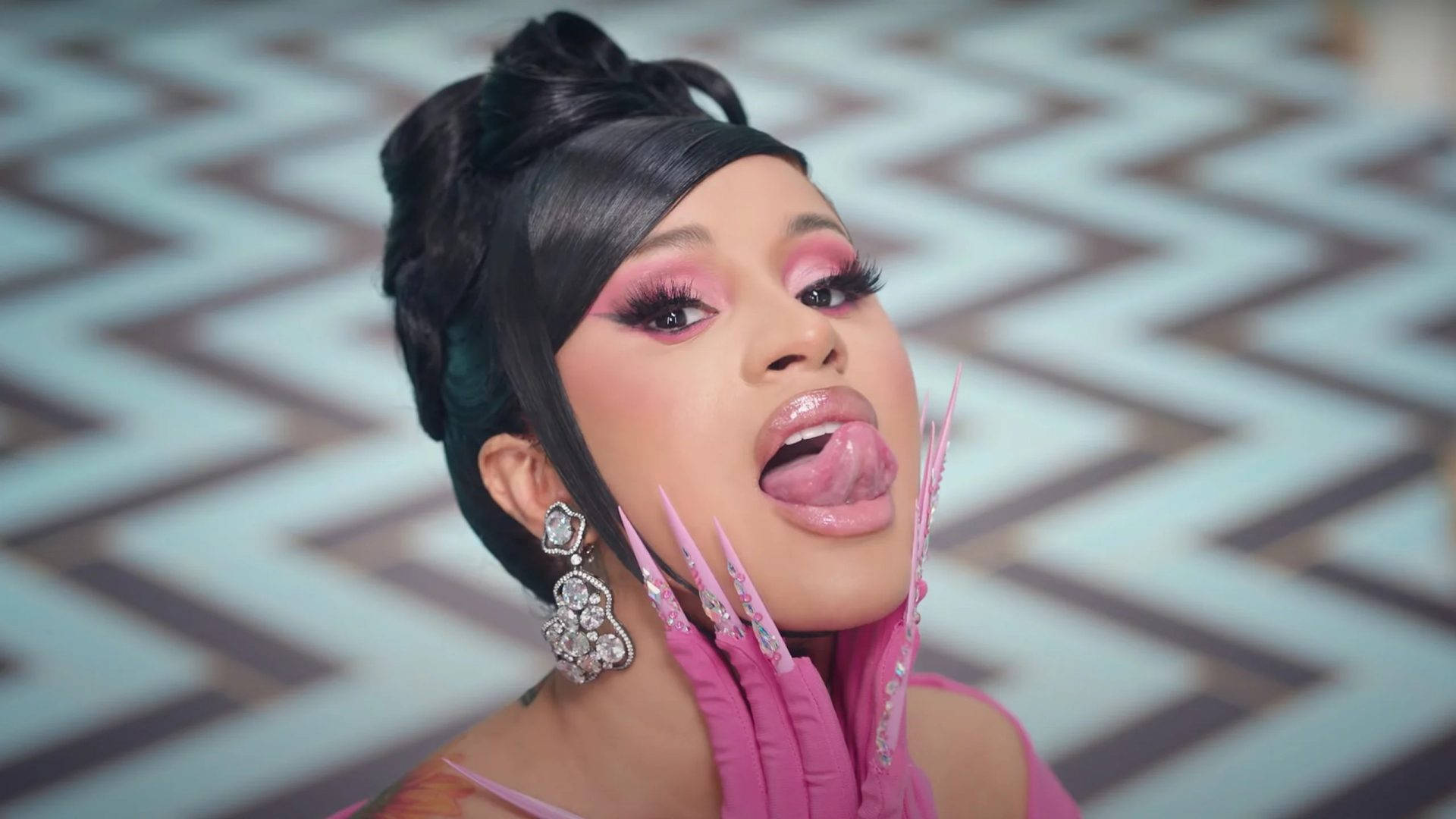 cardi 桌布 壁紙 — 一位魅力四射的女性，化著大膽的粉紅色妝容，留著尖銳的粉紅色指甲，在鋸齒紋背景前伸出舌頭。