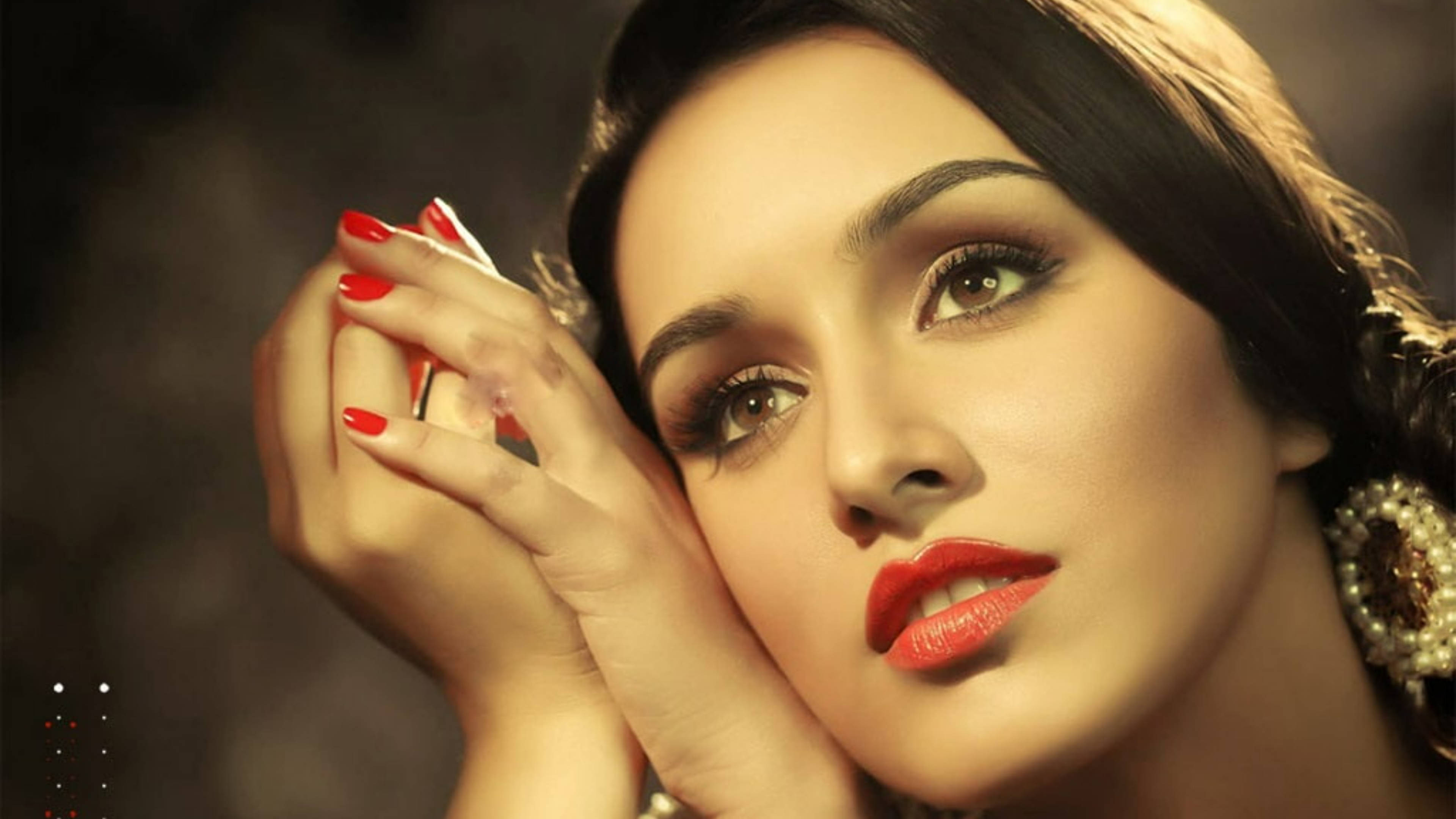 Shraddha Kapoor 桌布 壁紙 — 一位魅力四射的女性，擁有鮮豔的紅唇和紅指甲，在黑暗煙霧繚繞的背景前手持香水瓶。