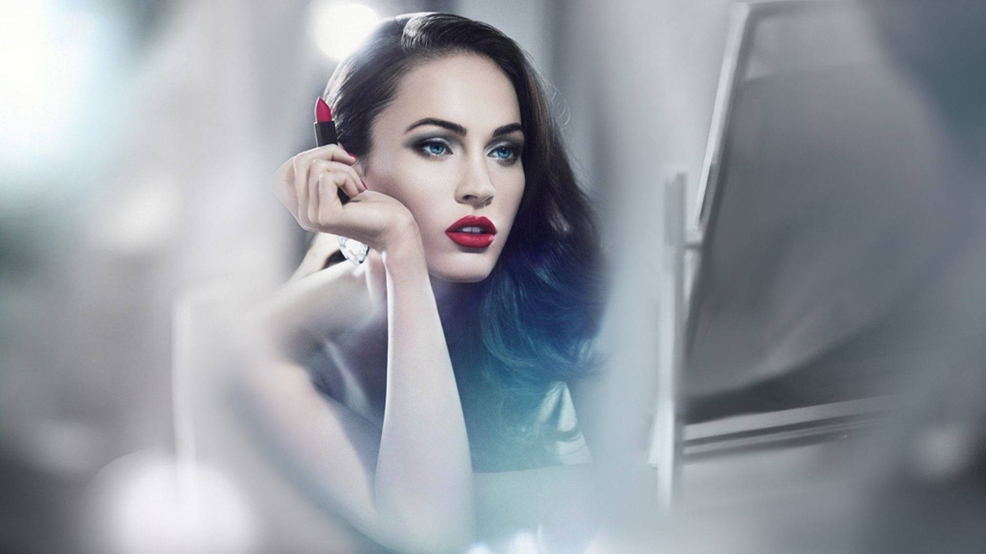 Megan Fox 桌布 壁紙 — 一位魅力四射的女性，擁有鮮豔的紅唇和引人注目的藍眼睛，在柔和模糊的高調工作室中化妝。