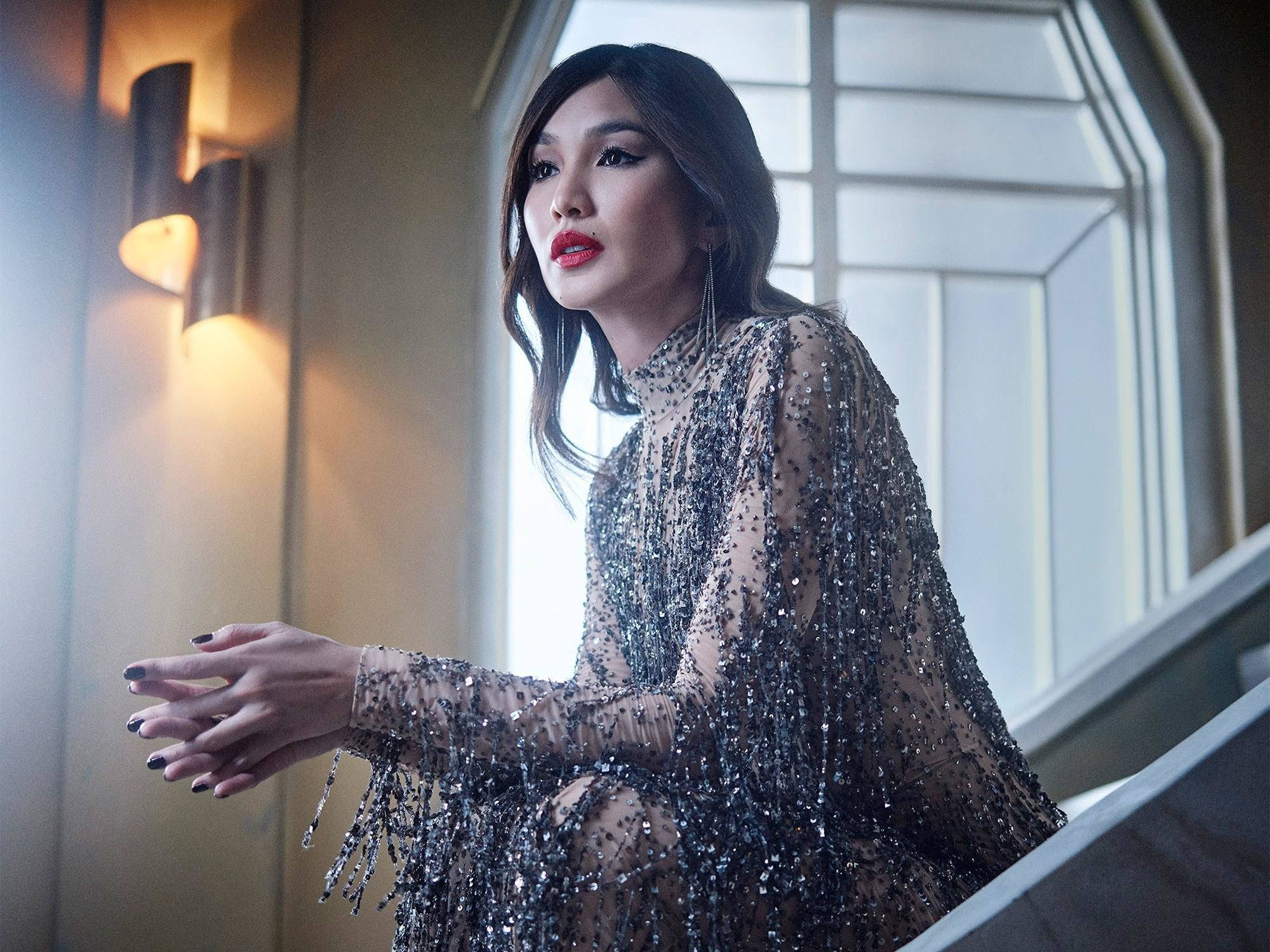 Gemma Chan 桌布 壁紙 — 一位魅力四射的女性身穿閃亮銀色禮服，優雅地坐在沐浴在溫暖環境光線中的樓梯上。
