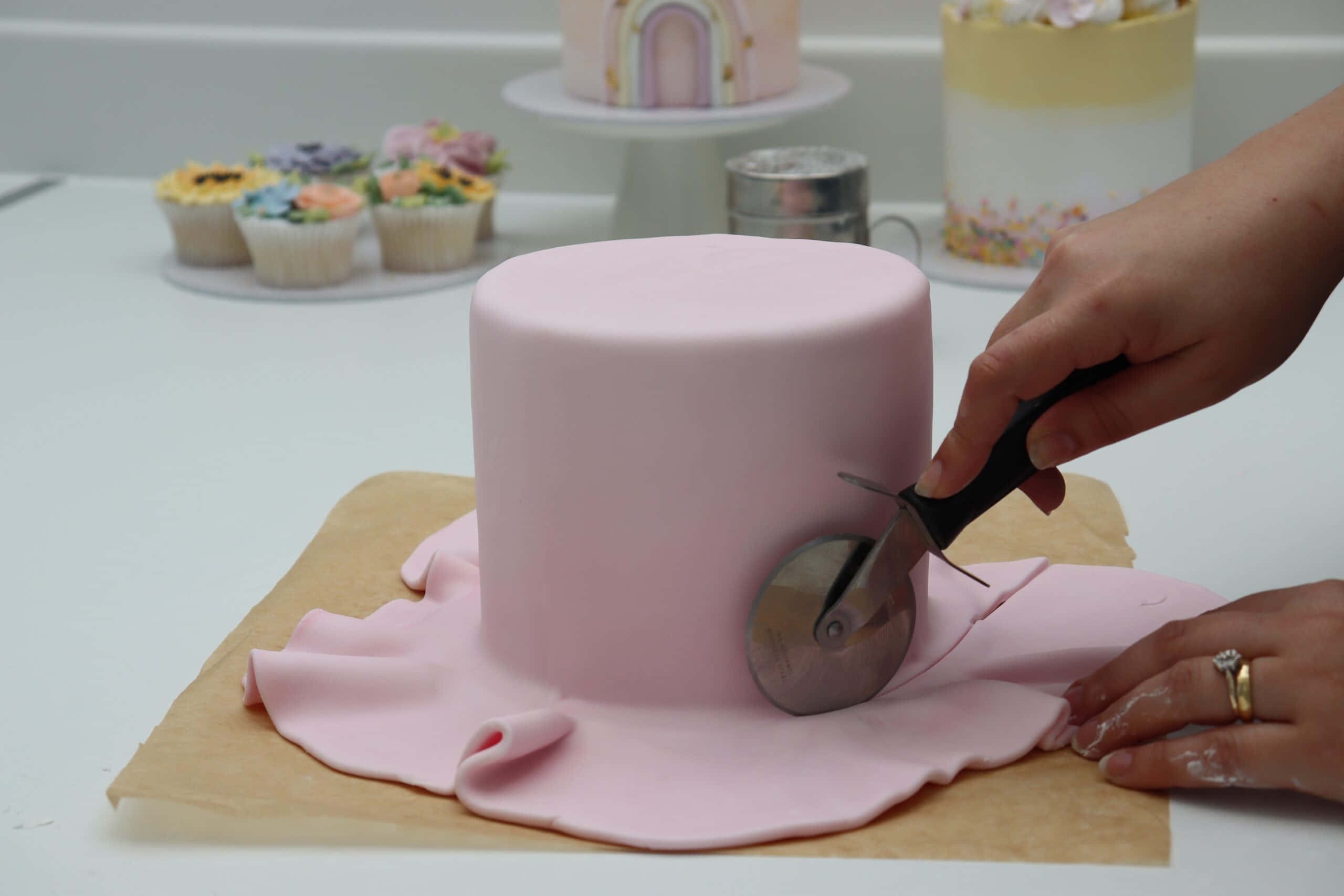 Cake Fondant 桌布 壁紙 — 一位麵包師傅用披薩切刀將烘焙紙上圓形蛋糕的平滑粉紅色翻糖切掉。