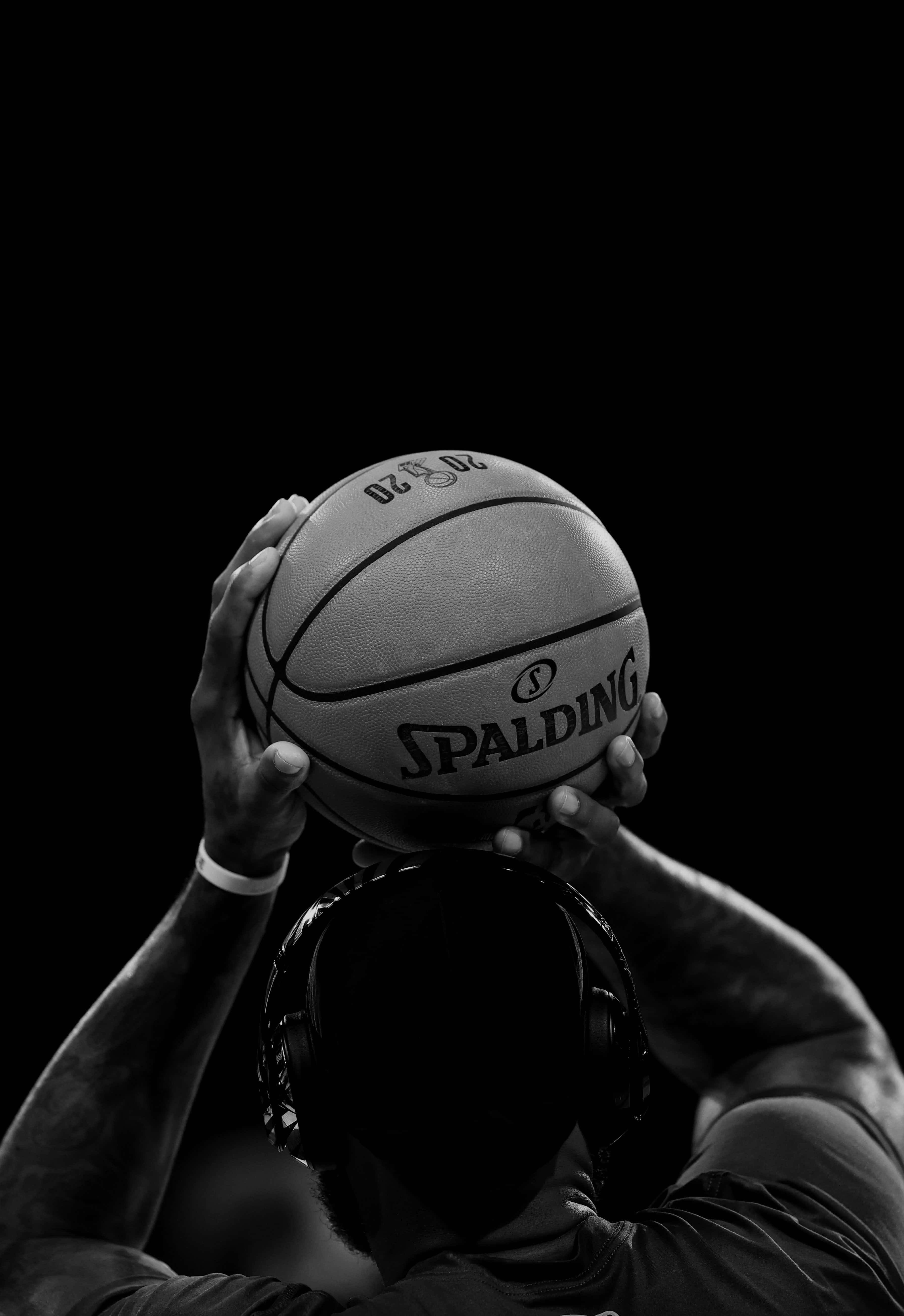 籃球 桌布 壁紙 — 一位黑白籃球運動員在深色背景上將 Spalding 球舉過頭頂。