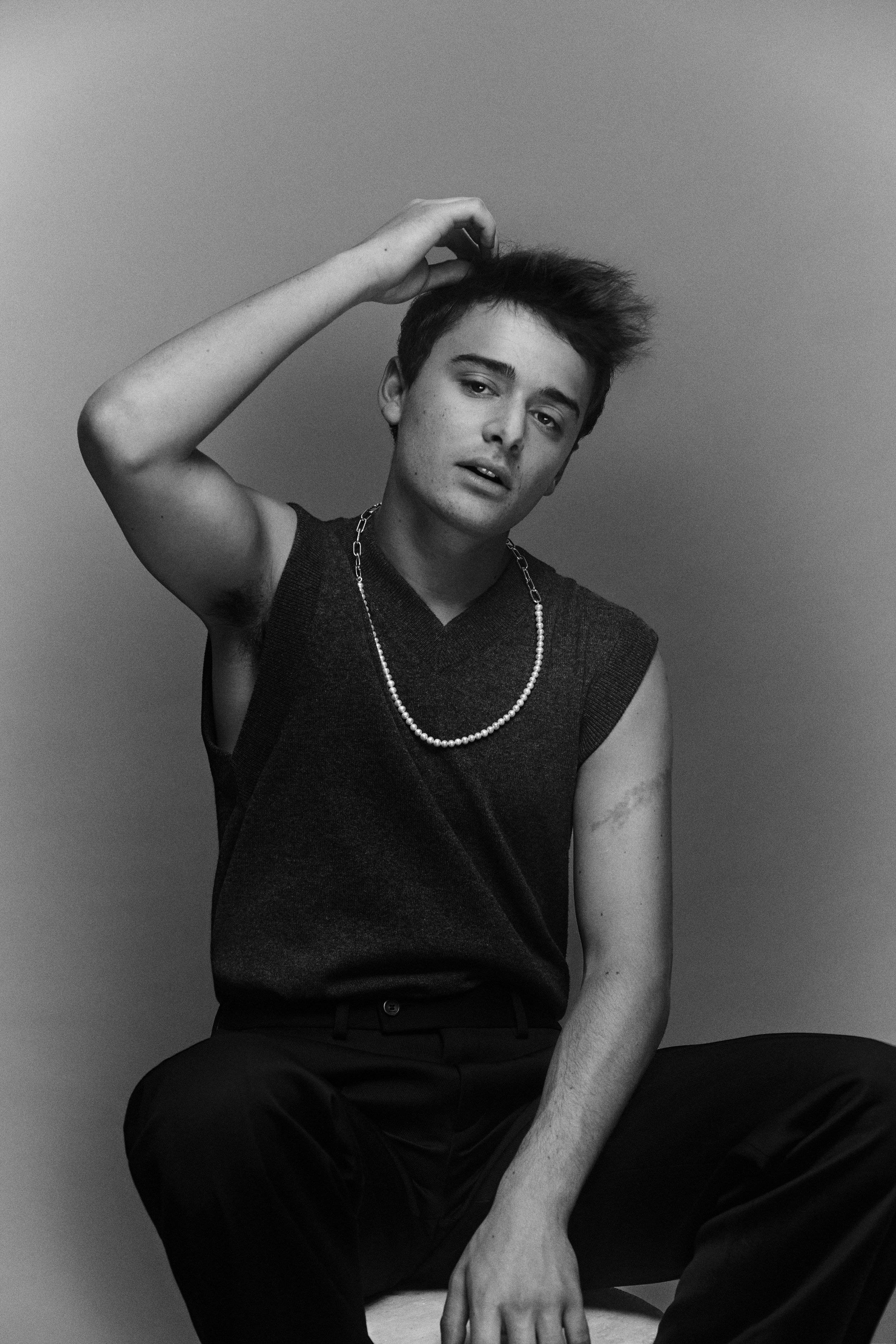 Fashion Model 桌布 壁紙 — 一位黑白風格的年輕男子隨意地坐著整理頭髮，戴著珍珠項鍊和無袖上衣。