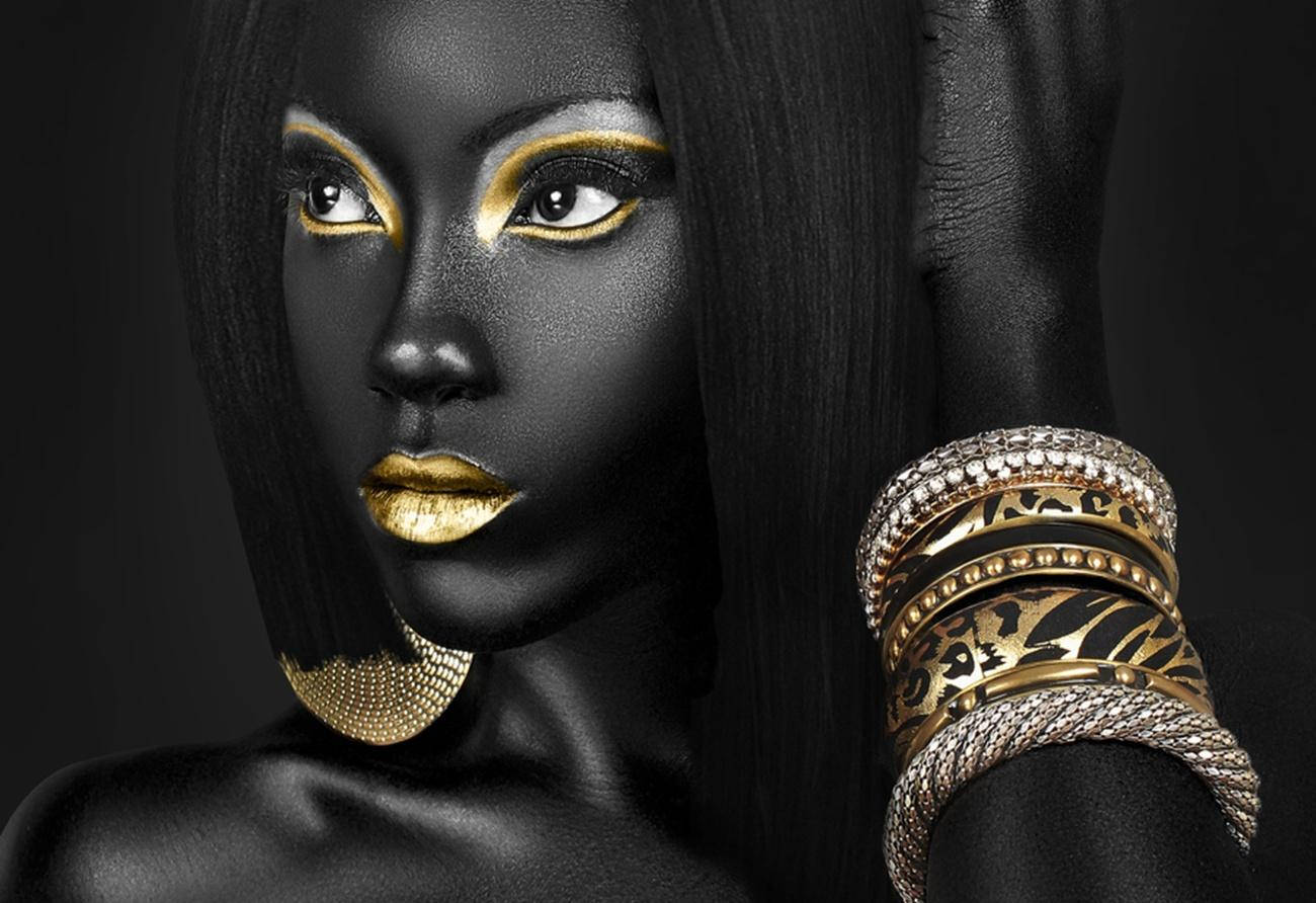 Black Girl 桌布 壁紙 — 一位黑皮膚、金色化妝的女性，在深色背景前佩戴華麗的金飾擺姿勢。