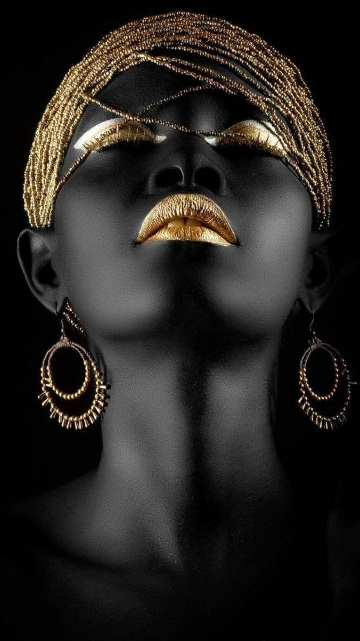 Beautiful Woman 桌布 壁紙 — 一位黑皮膚、金色化妝的女性，在飾有金色珠子和耳環的黑色背景下向上凝視。
