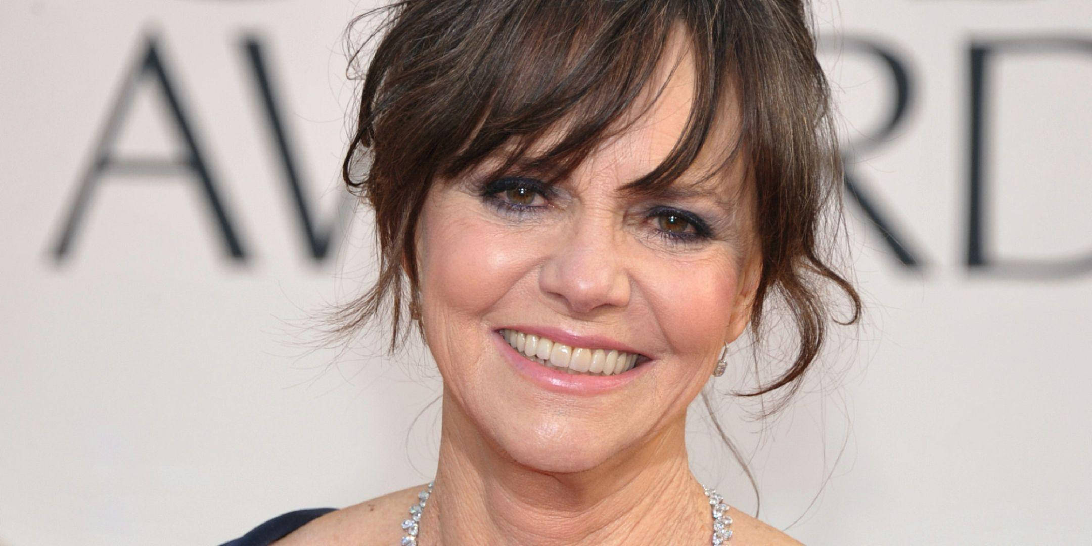 Celebrity 桌布 壁紙 — 一位黑髮、戴著鑽石珠寶的微笑女士在頒獎活動中，以白色背景和粗體字為背景擺姿勢。