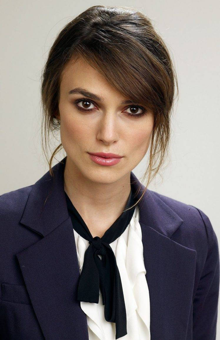 Keira Knightley 桌布 壁紙 — 一位黑髮、眼神銳利的女性特寫肖像，身穿海軍藍西裝外套，內搭白色襯衫，繫著黑色蝴蝶結。