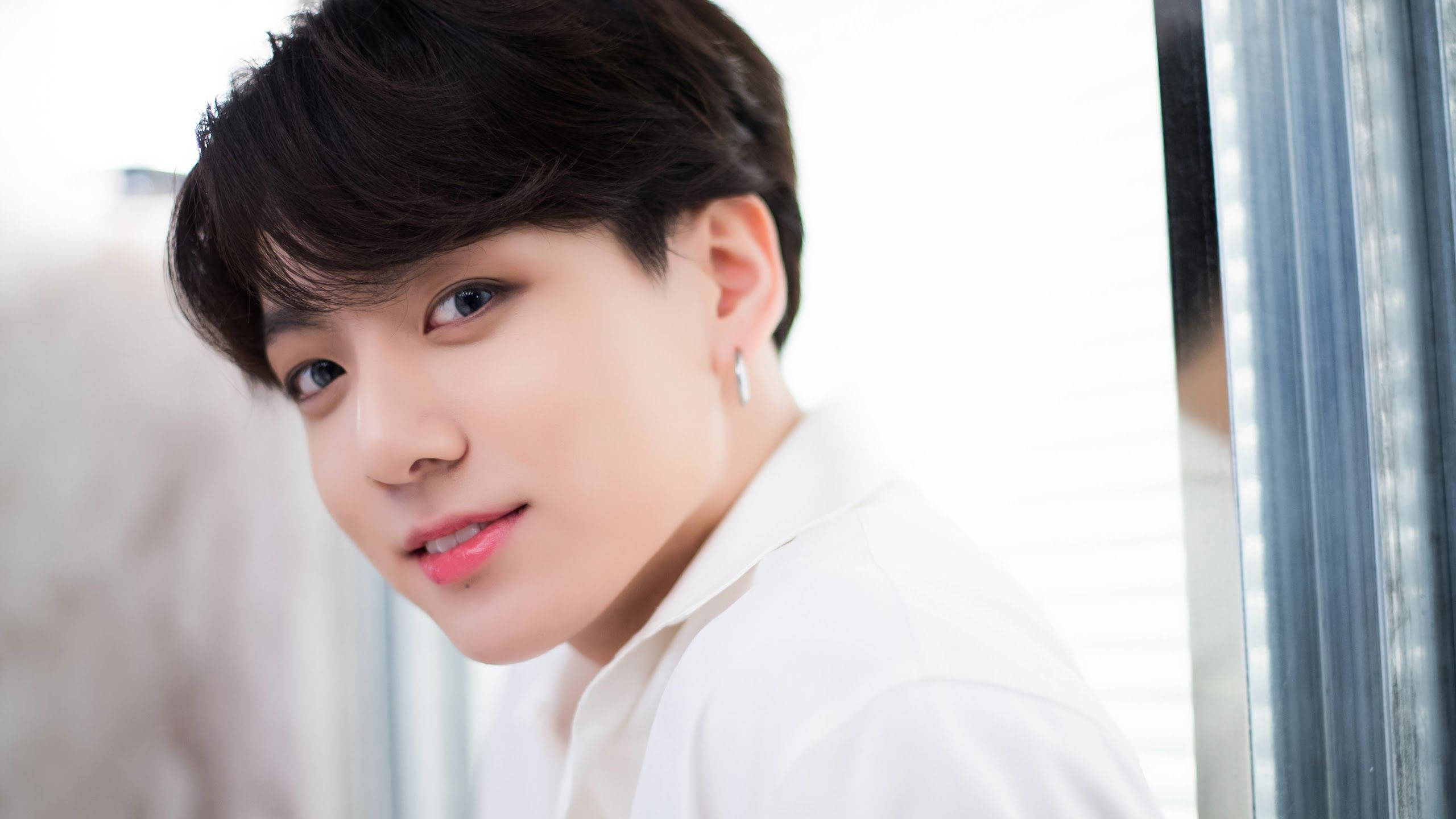 Jungkook 桌布 壁紙 — 一位黑髮、身穿白襯衫的年輕男子，在帶有百葉窗的窗戶附近溫柔地凝視著相機。