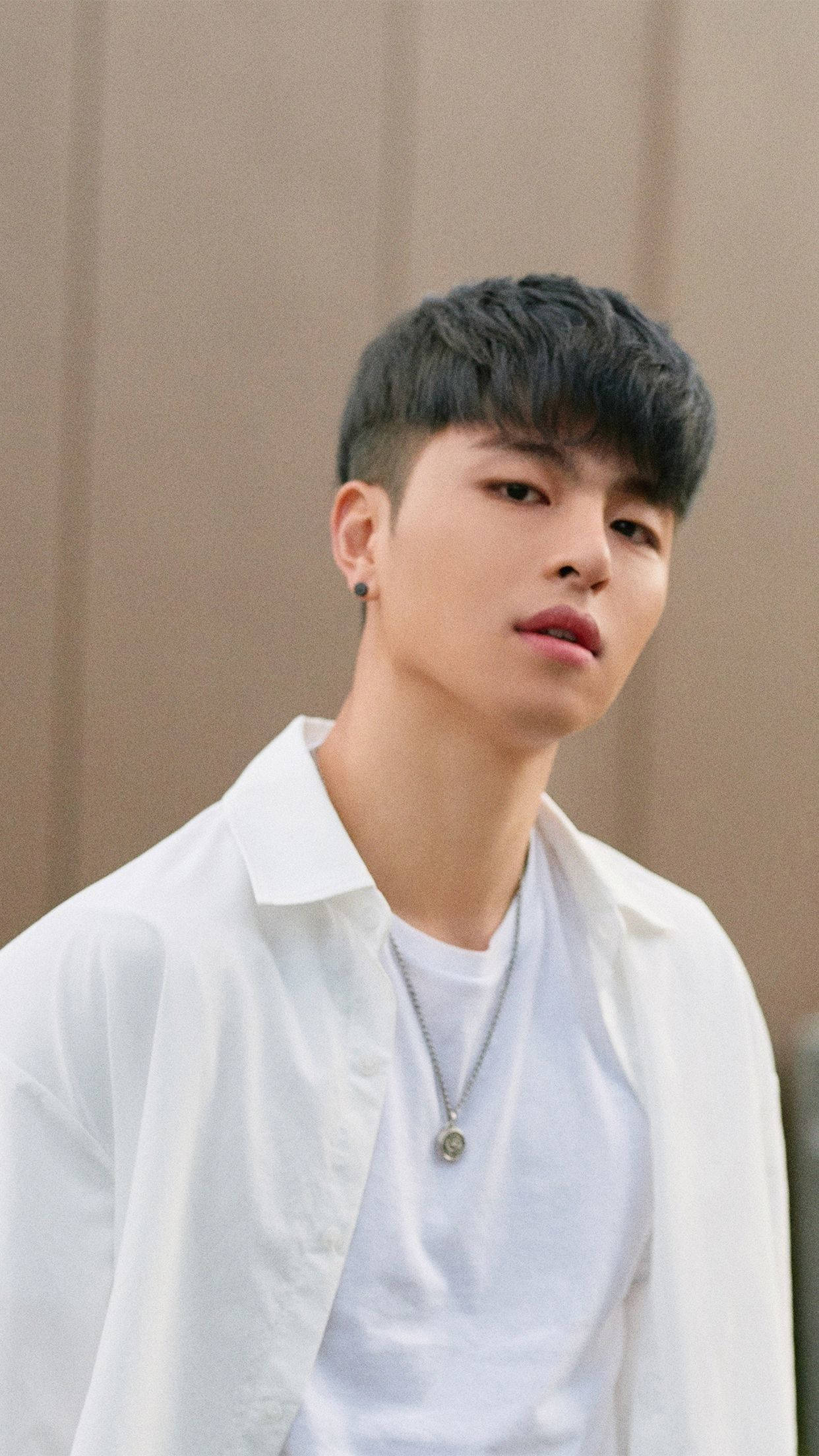 Ikon 桌布 壁紙 — 一位黑髮、身穿白襯衫的年輕男子，若有所思地凝視著中性色調的牆壁。