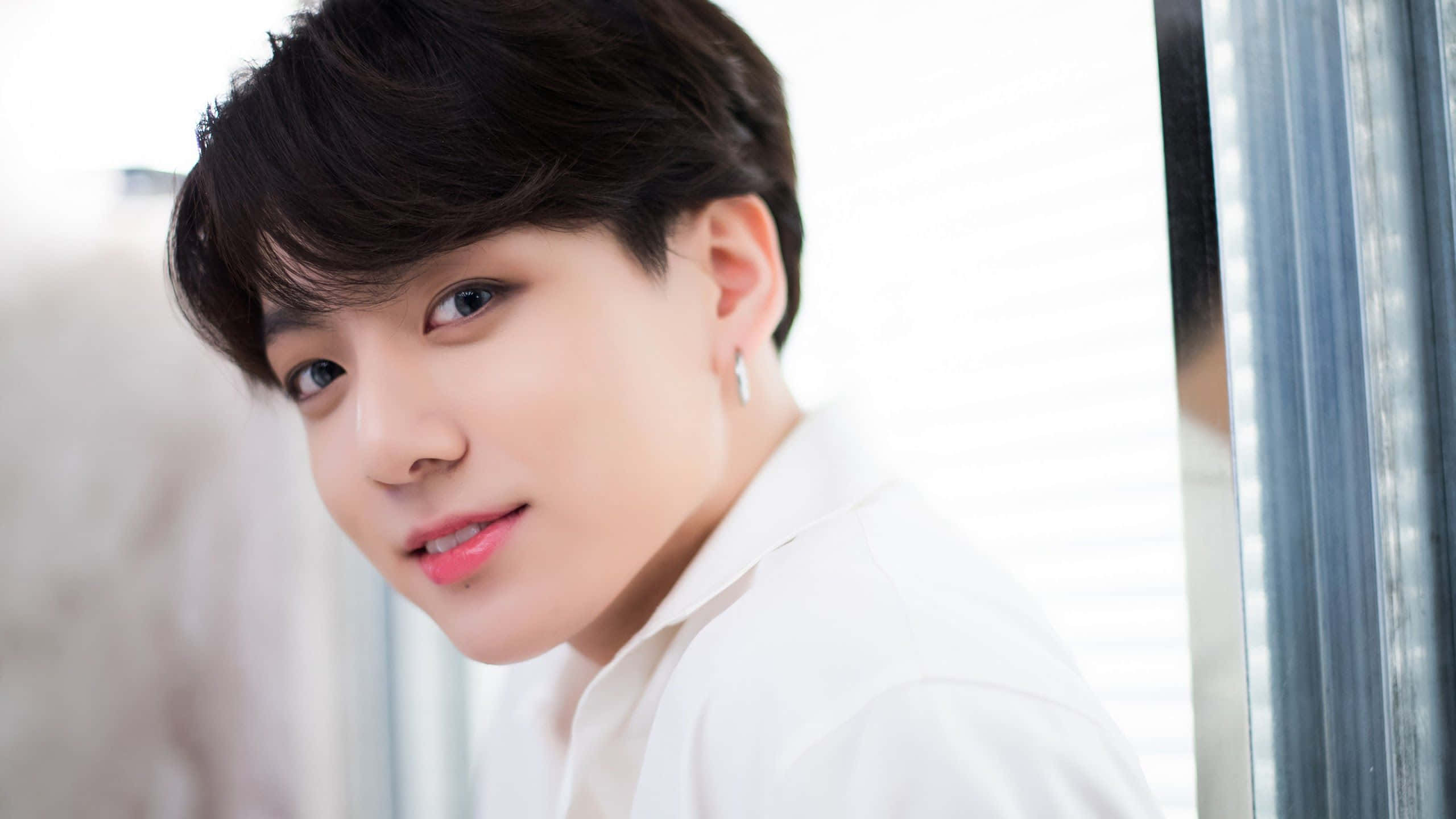Jungkook 桌布 壁紙 — 一位黑髮、身穿白襯衫的年輕男子在帶有百葉窗的窗戶旁溫柔地凝視著相機。