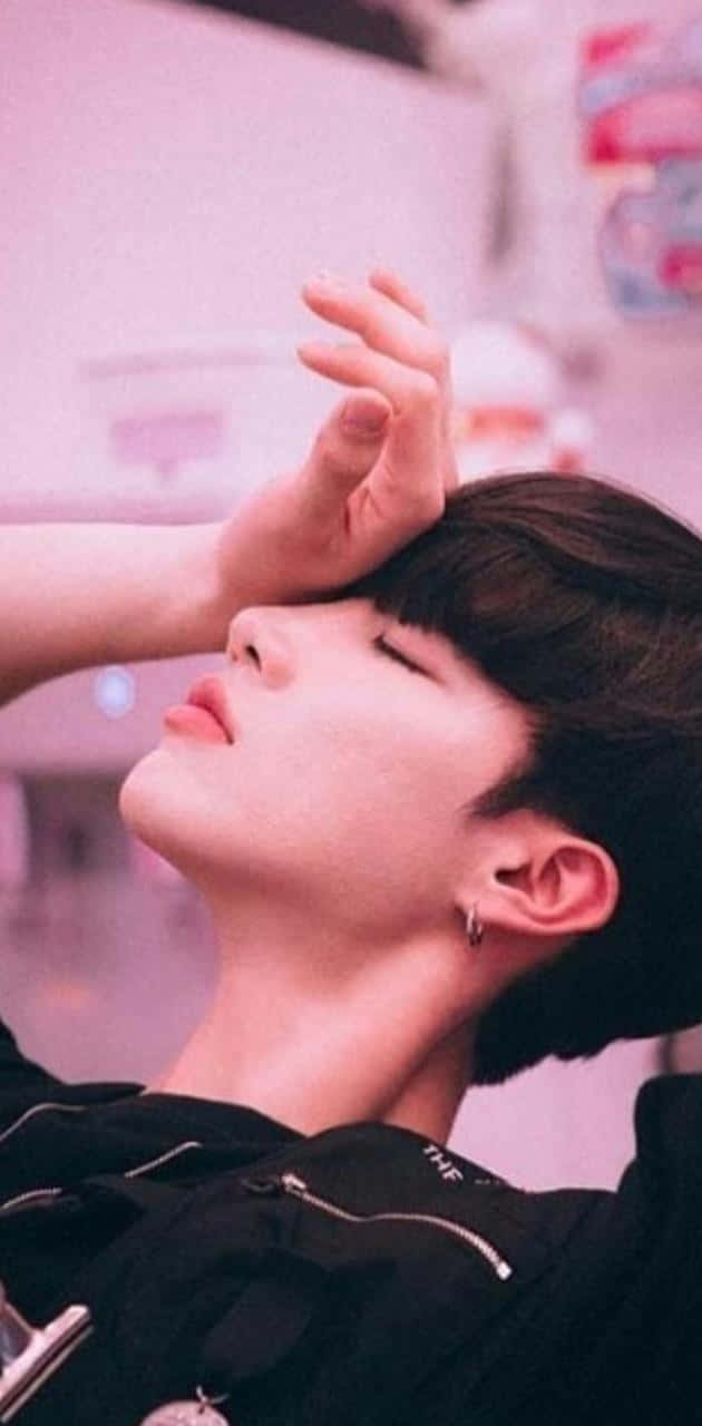 男孩 桌布 壁紙 — 一位黑髮、身穿黑色外套的年輕男子，頭向後仰，閉著眼睛，手放在額頭上，背景是柔和的粉紅色。