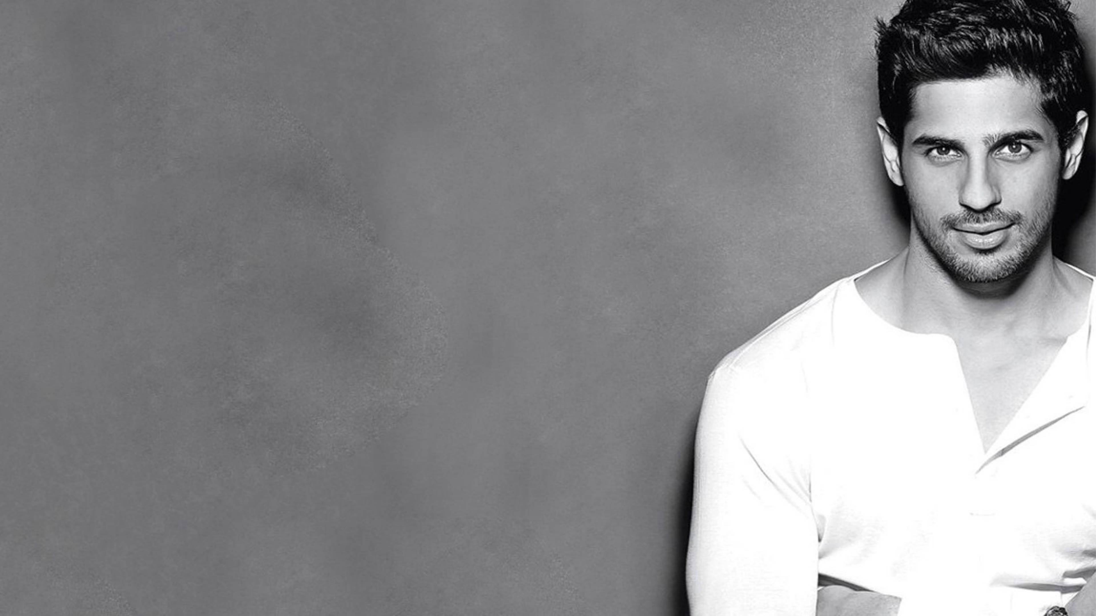 Sidharth Malhotra 桌布 壁紙 — 一位黑髮、鬍渣的俊男穿著白襯衫，在紋理灰色背景前的黑白肖像。