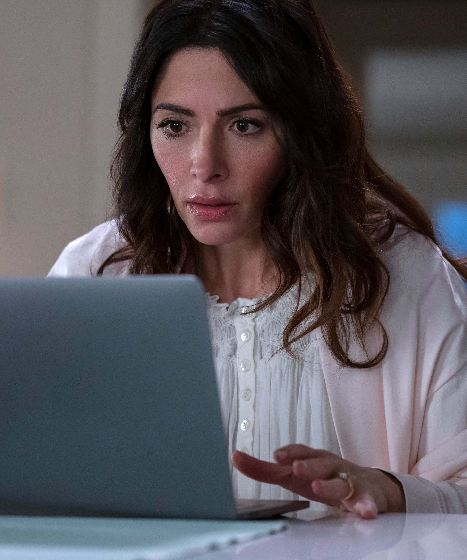 sarah shahi 桌布 壁紙 — 一位黑髮女子身穿白色襯衫，神情專注地盯著筆記型電腦螢幕，面露憂色。