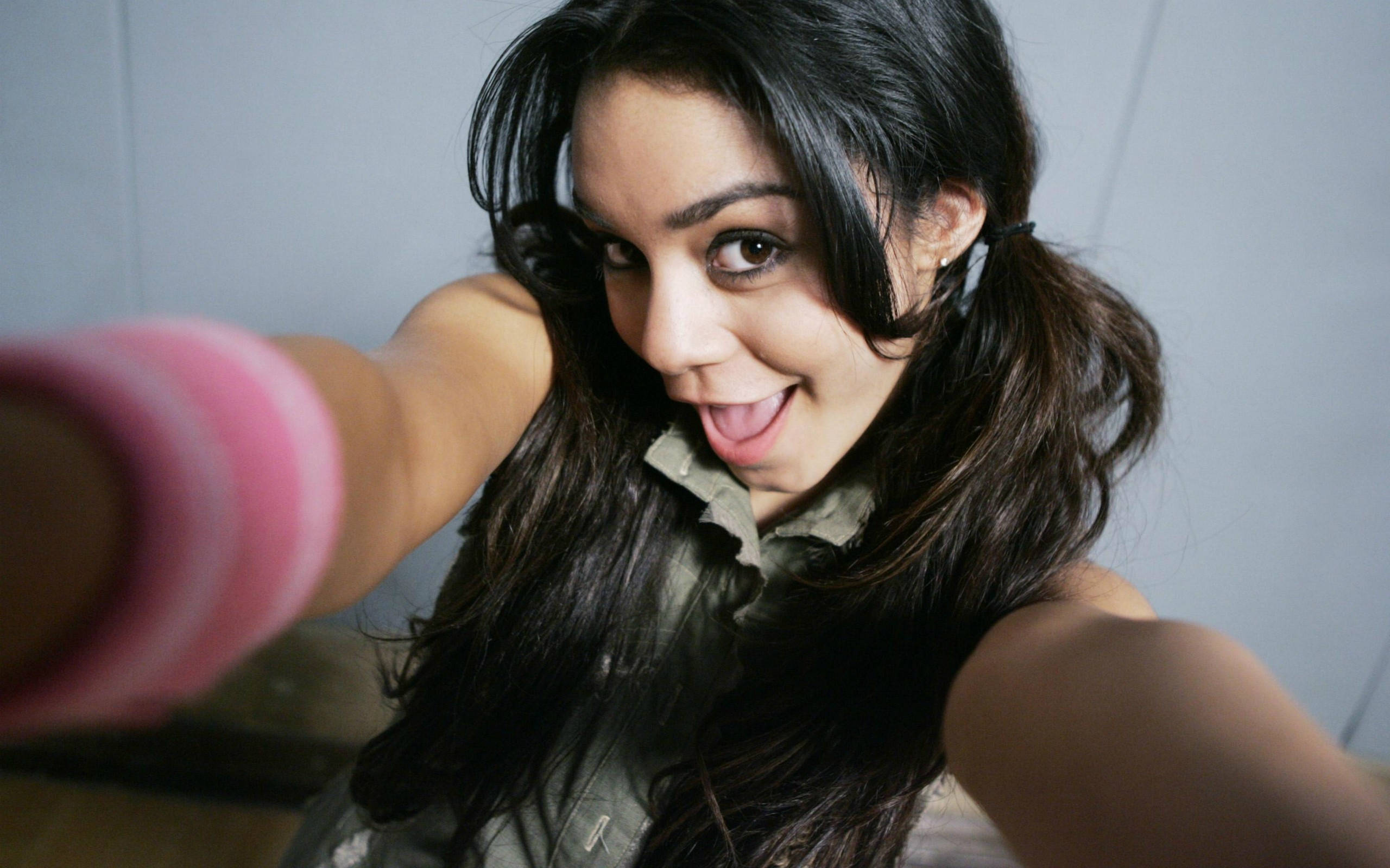 Vanessa Hudgens 桌布 壁紙 — 一位黑髮年輕女子一邊用粉紅色條紋手機自拍，一邊頑皮地伸出舌頭。