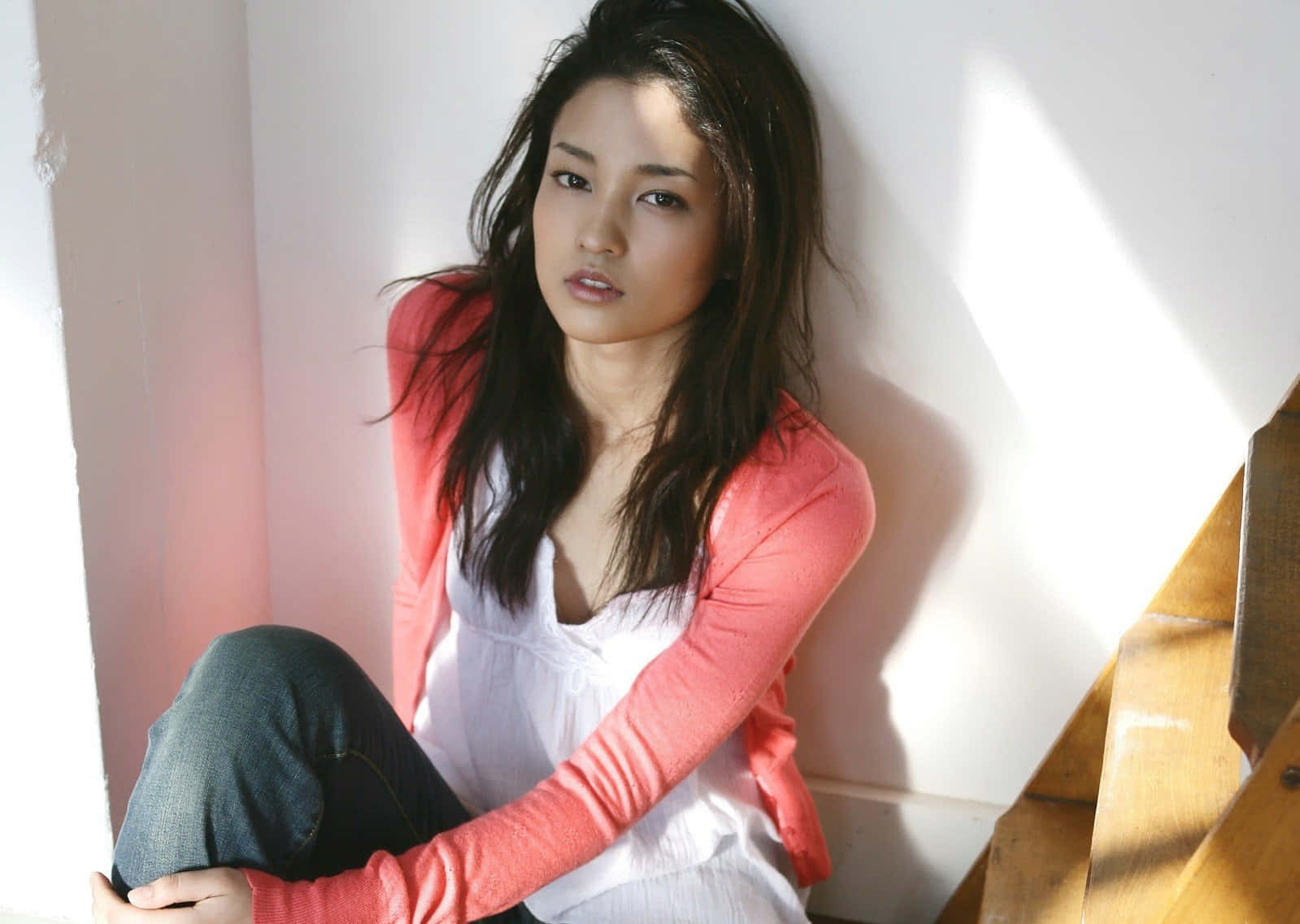 Japanese Women 桌布 壁紙 — 一位黑髮年輕女性坐在木樓梯上，沐浴在溫暖的陽光中，在白牆上投下柔和陰影。