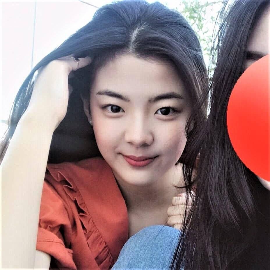 Lia 桌布 壁紙 — 一位黑髮年輕女性微笑著輕觸頭髮，身穿鏽紅色上衣和藍色牛仔褲。