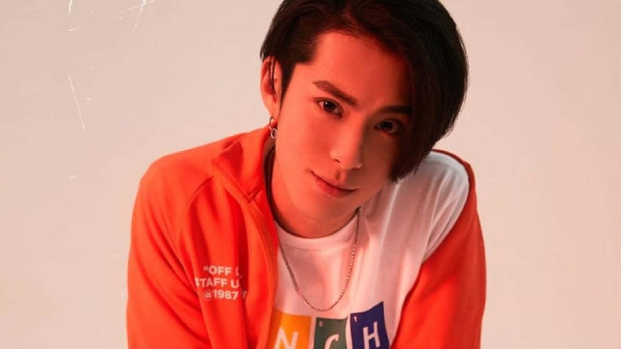 Dylan Wang 桌布 壁紙 — 一位黑髮年輕男子，帶著微妙笑容，身穿橙色和白色連帽衫，背景為純白色。