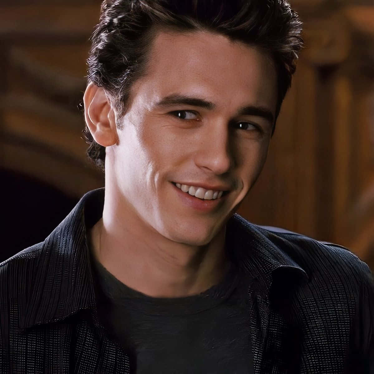 Harry Osborn 桌布 壁紙 — 一位黑髮年輕男子在昏暗的木質室內溫暖地微笑。