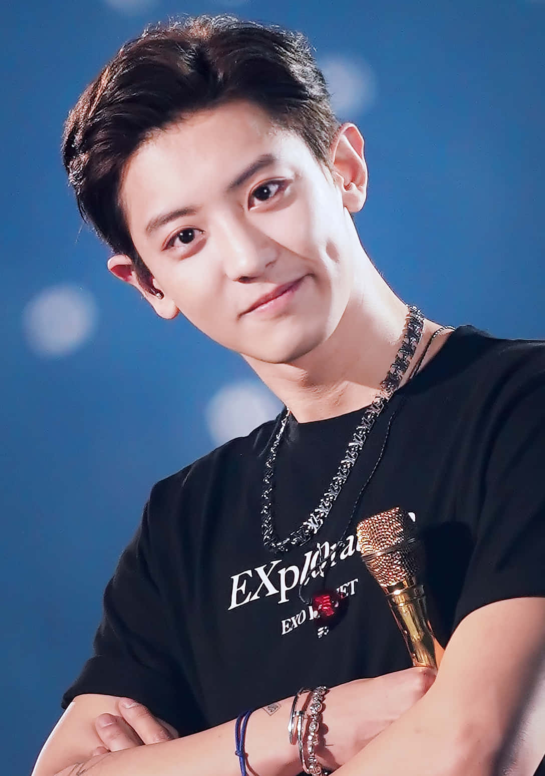 EXO 桌布 壁紙 — 一位黑髮年輕男子帶著溫柔的微笑，在柔和的藍色背景與散景燈光下握著麥克風。