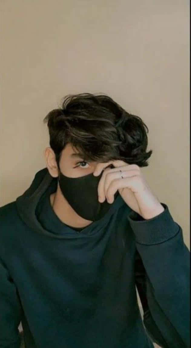 Instagram Profile 桌布 壁紙 — 一位黑髮年輕男子戴著黑色口罩，用手輕輕掀起口罩，露出一隻眼睛，背景是純色米色牆壁。