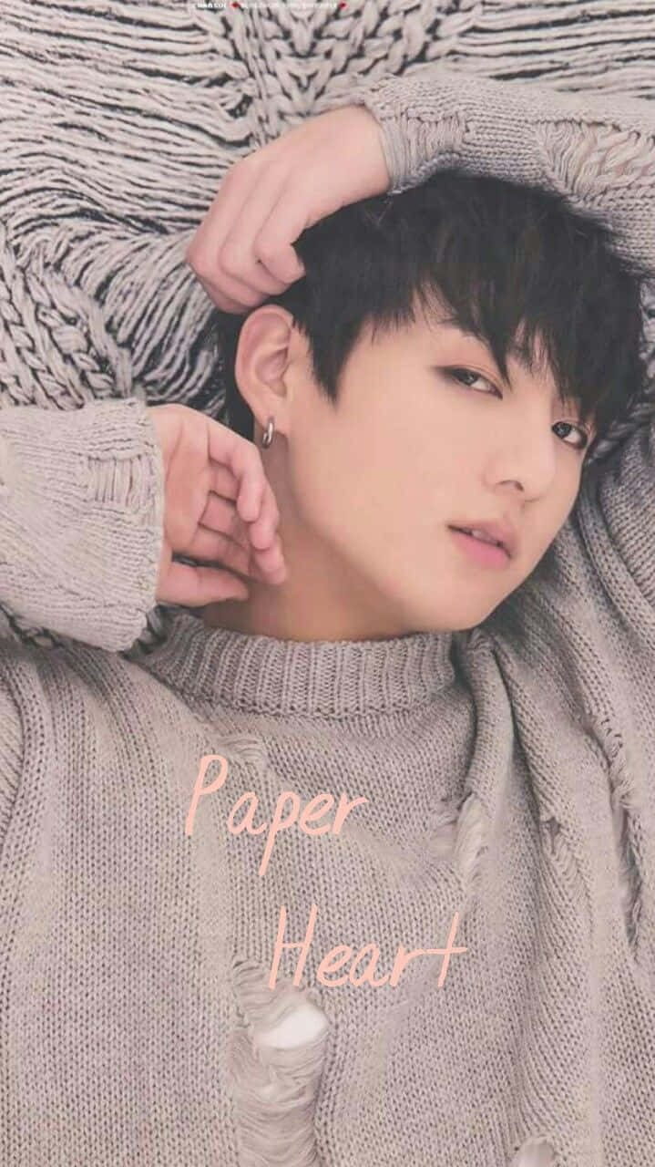 Jungkook 桌布 壁紙 — 一位黑髮年輕男子放鬆地躺在質感灰色針織毛衣上，搭配同色系毛毯，溫柔地凝視鏡頭。