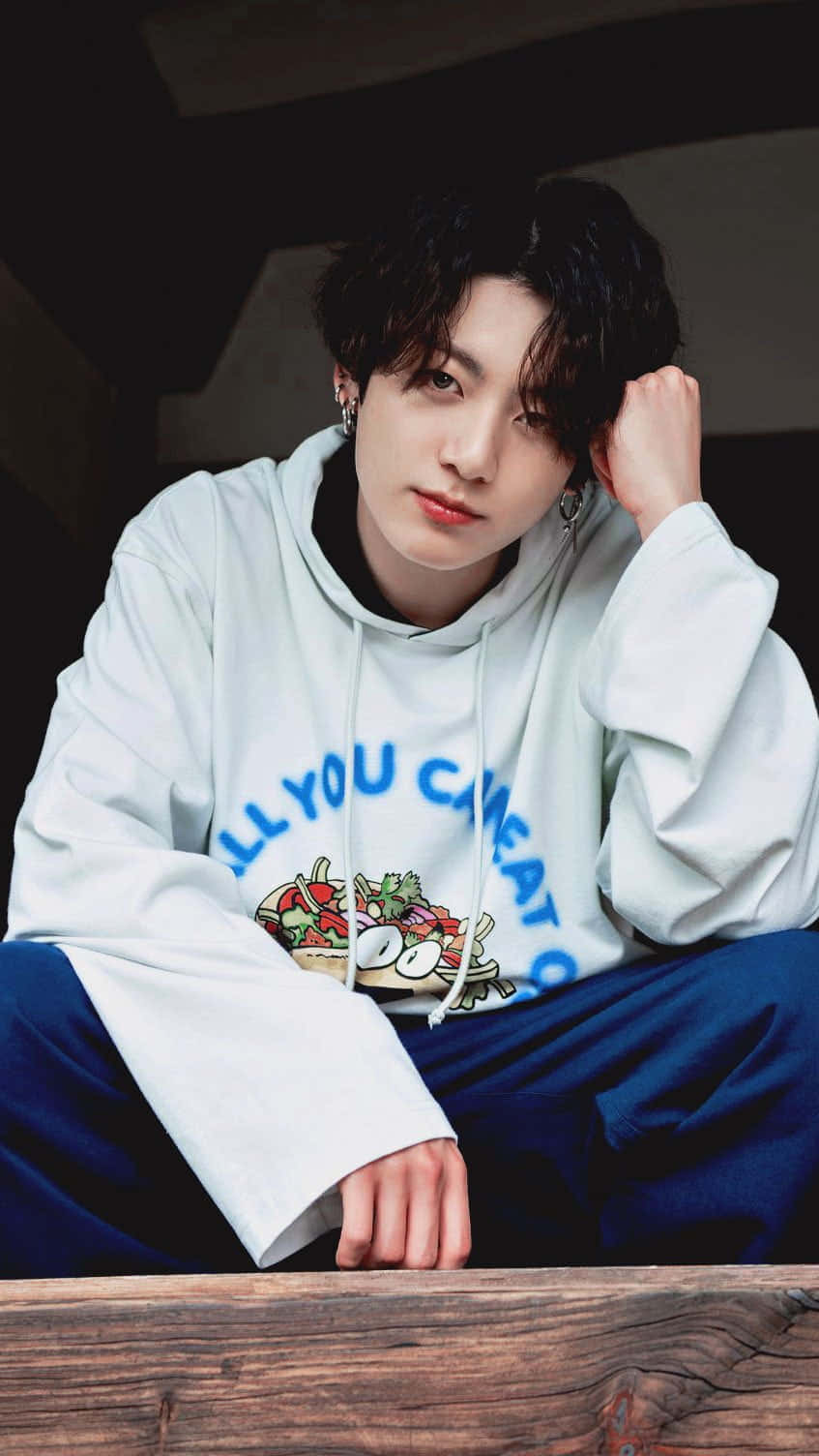 Jungkook 桌布 壁紙 — 一位黑髮年輕男子穿著帶有沙拉圖案的連帽衫，隨意地坐著，直視鏡頭。