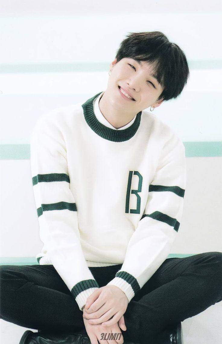 Suga Bts 桌布 壁紙 — 一位黑髮年輕男子穿著白綠條紋毛衣，盤腿坐在極簡條紋背景前，露出溫暖的笑容。