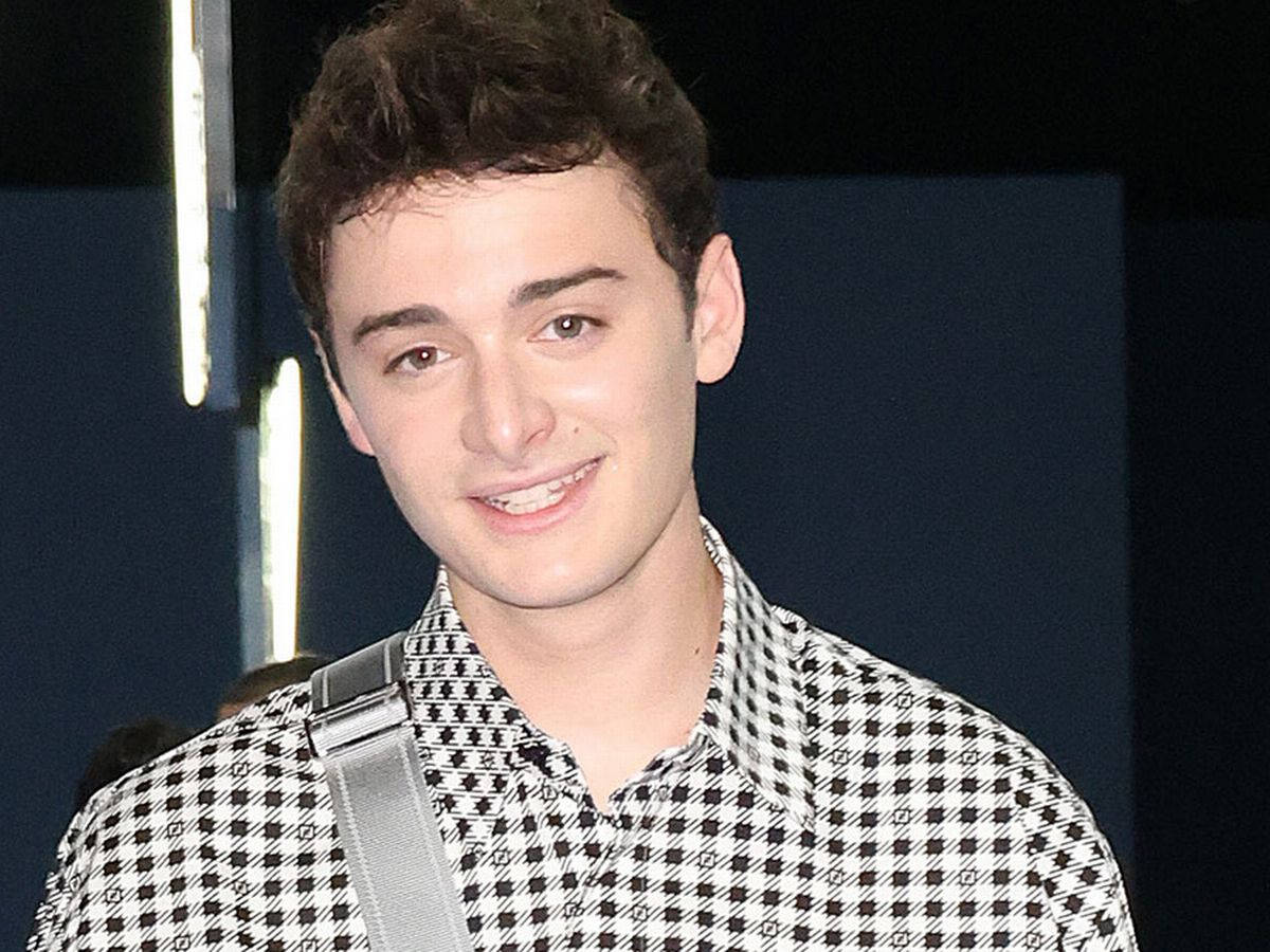 Celebrity 桌布 壁紙 — 一位黑髮年輕男子穿著黑白格紋襯衫，肩上掛著灰色肩帶，露出溫暖的笑容。