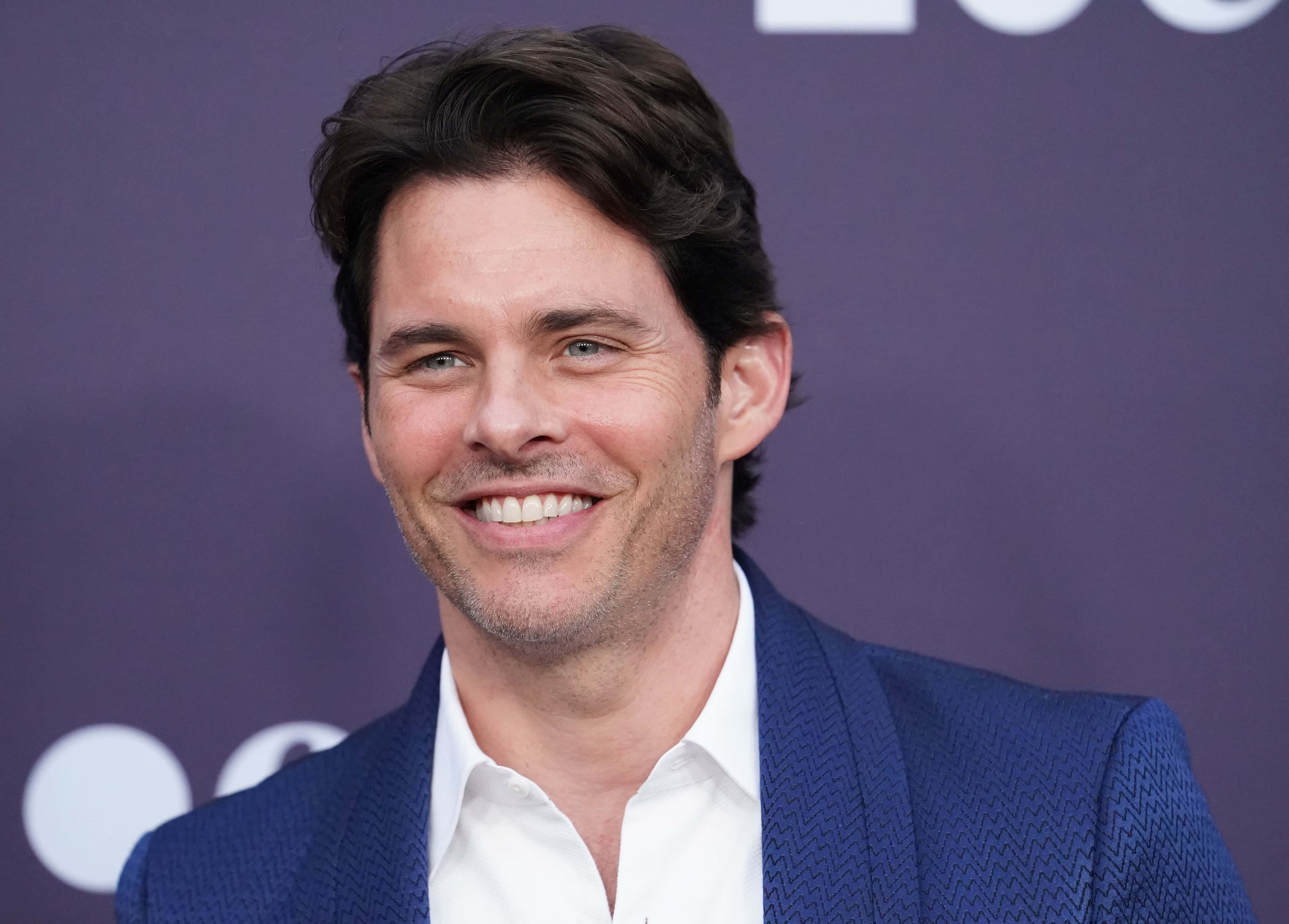 James Marsden 桌布 壁紙 — 一位黑髮微笑男士，在紫色背景前穿著藍色質感西裝外套，內搭白襯衫。