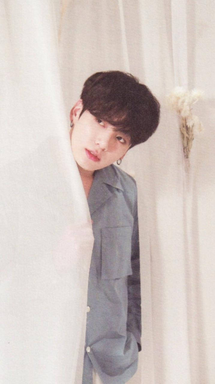 Jungkook Aesthetic 桌布 壁紙 — 一位黑髮戴耳環的年輕男子，穿著灰色襯衫，從柔軟的白色窗簾後探出頭來。