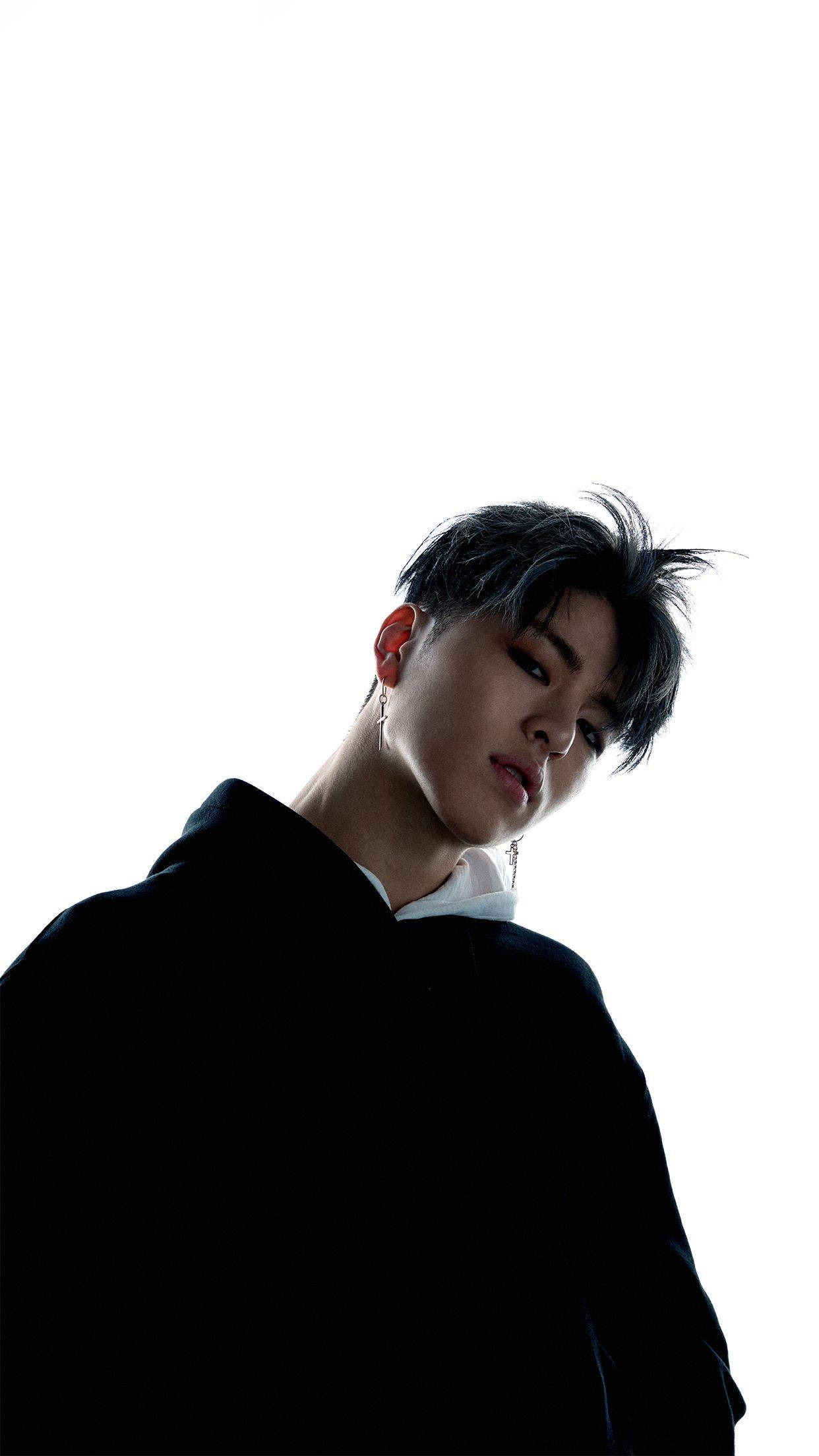 Ikon 桌布 壁紙 — 一位黑髮戴耳環的年輕男子，穿著黑色連帽衫，在純白背景前向下凝視。