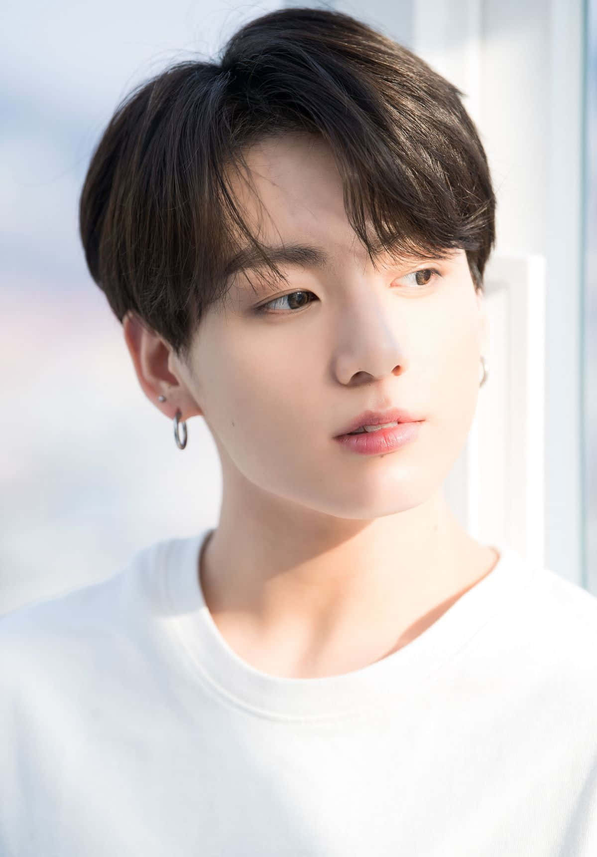 Jungkook 桌布 壁紙 — 一位黑髮戴著圈狀耳環的年輕男子，穿著白色T恤，在明亮的窗戶背景下若有所思地凝視著。
