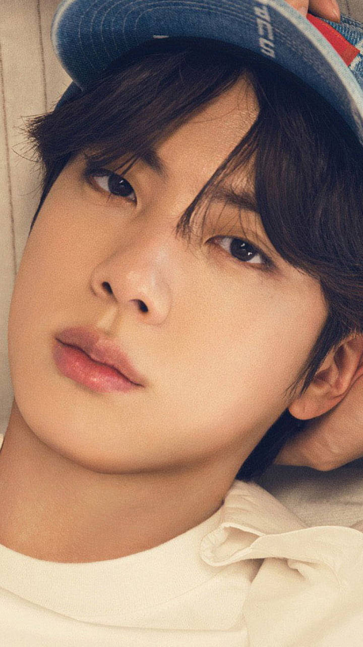 kim seok jin 桌布 壁紙 — 一位黑髮戴藍色帽子的年輕男子，頭靠淺色牆壁，溫柔地凝視鏡頭。